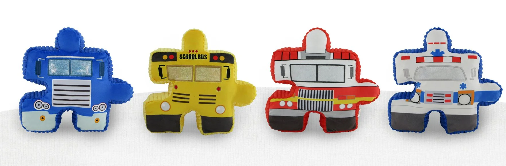 Four Pluzzles plush toys from the automotive series shaped like different emergency and transportation vehicles, including a blue police car, a yellow school bus, a red fire truck, and a white ambulance with blue accents.