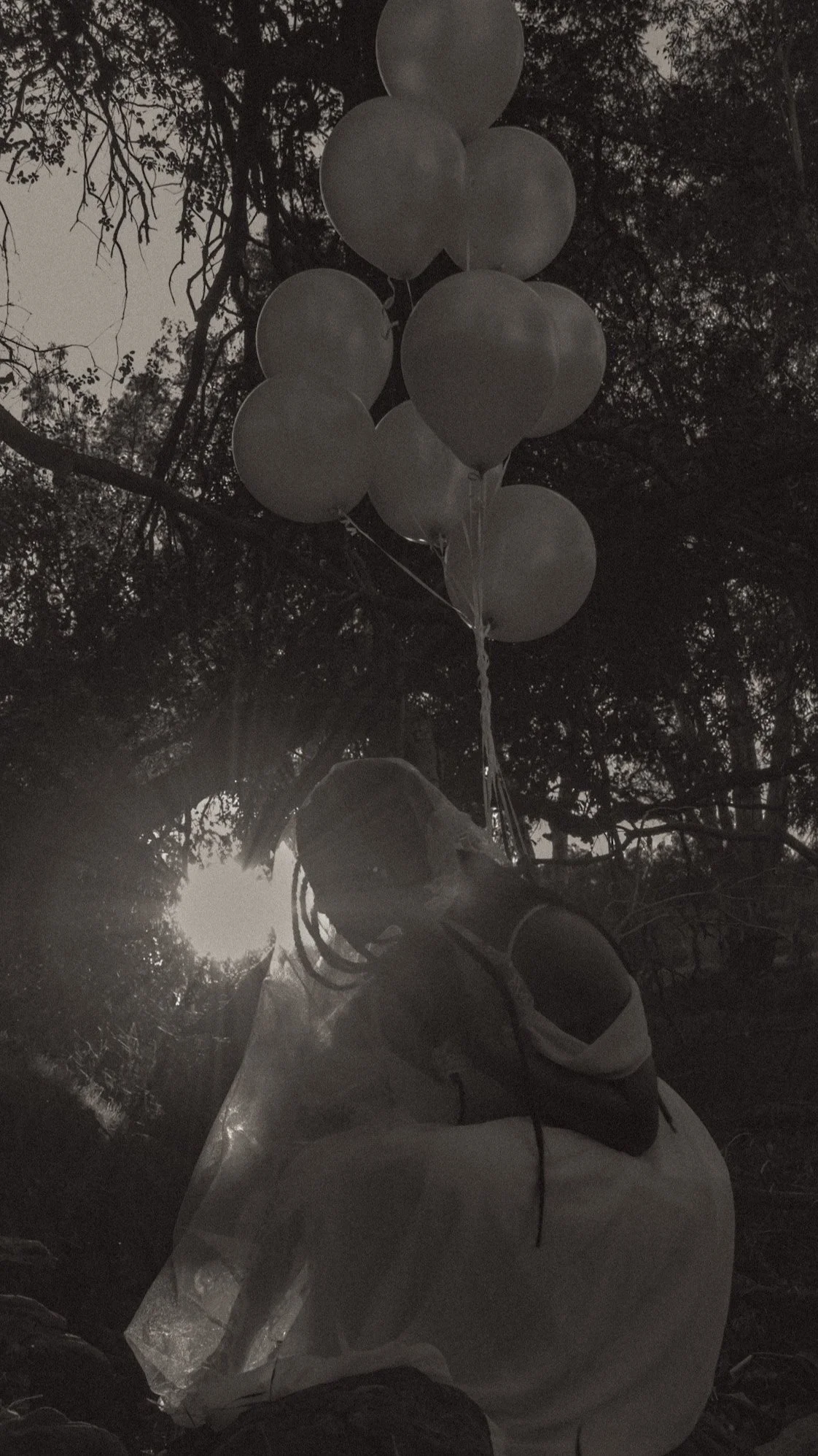 A girl in a light-colored dress holding a bunch of white balloons outdoors during sunset.