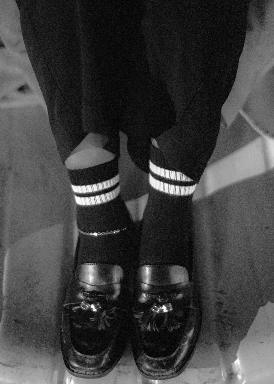 Person wearing black and white striped socks, black shoes, and dark pants, standing between two seats.