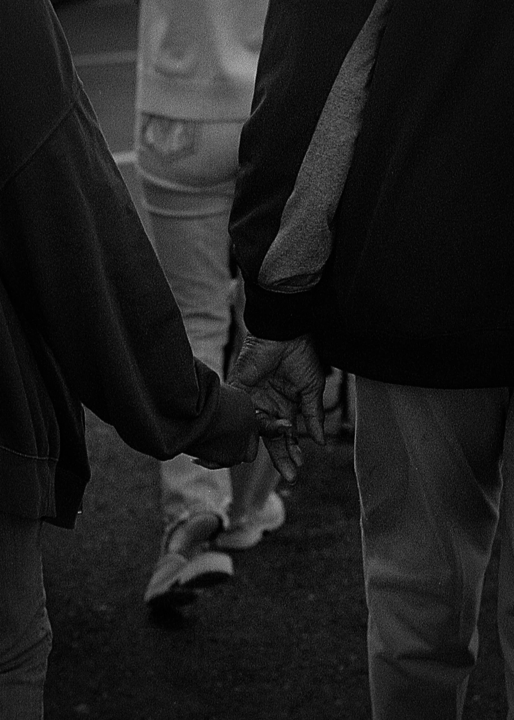 Two people holding hands in a black and white photo, with a crowd of people in the background.