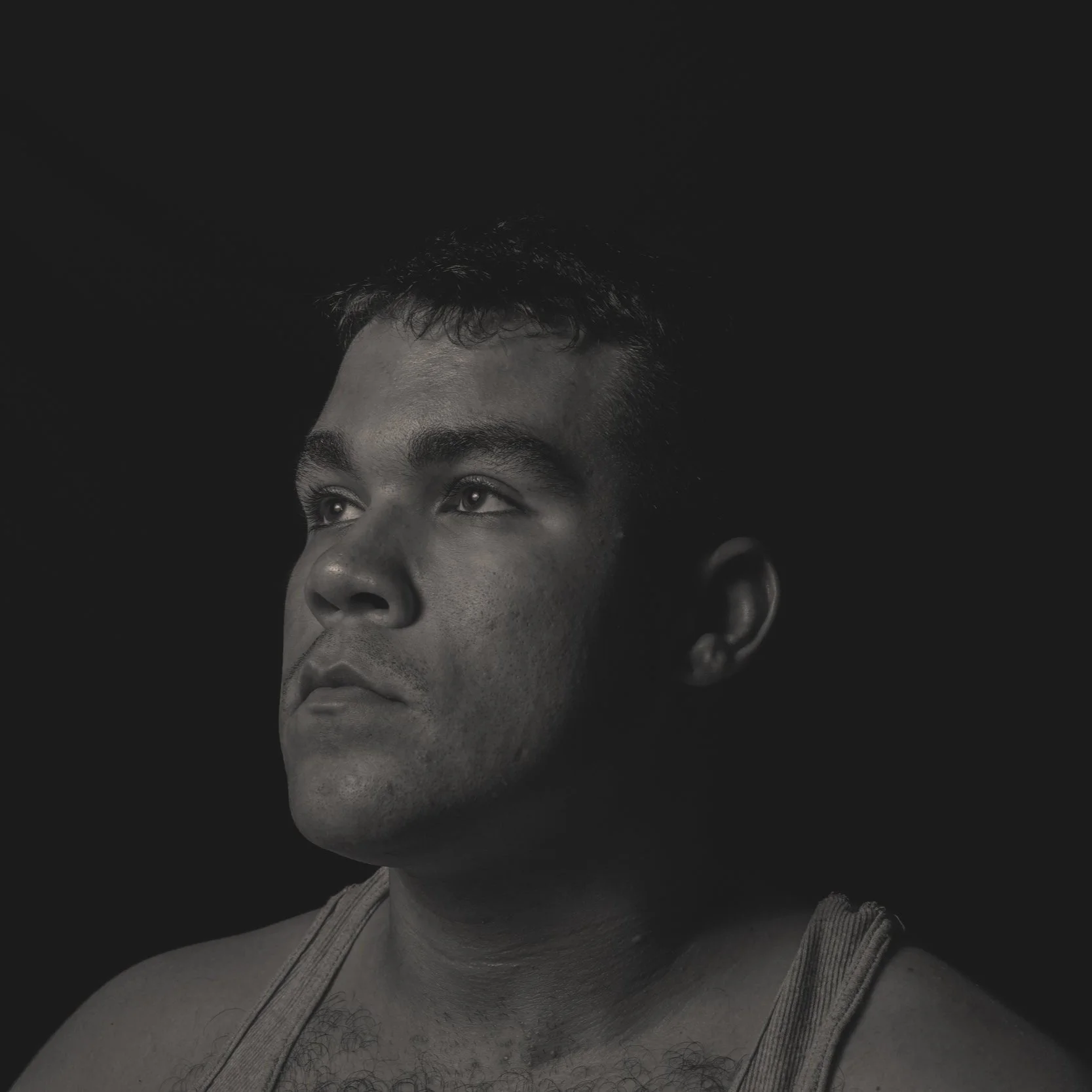 Black and white portrait of a man with short dark hair, gazing upward against a dark background