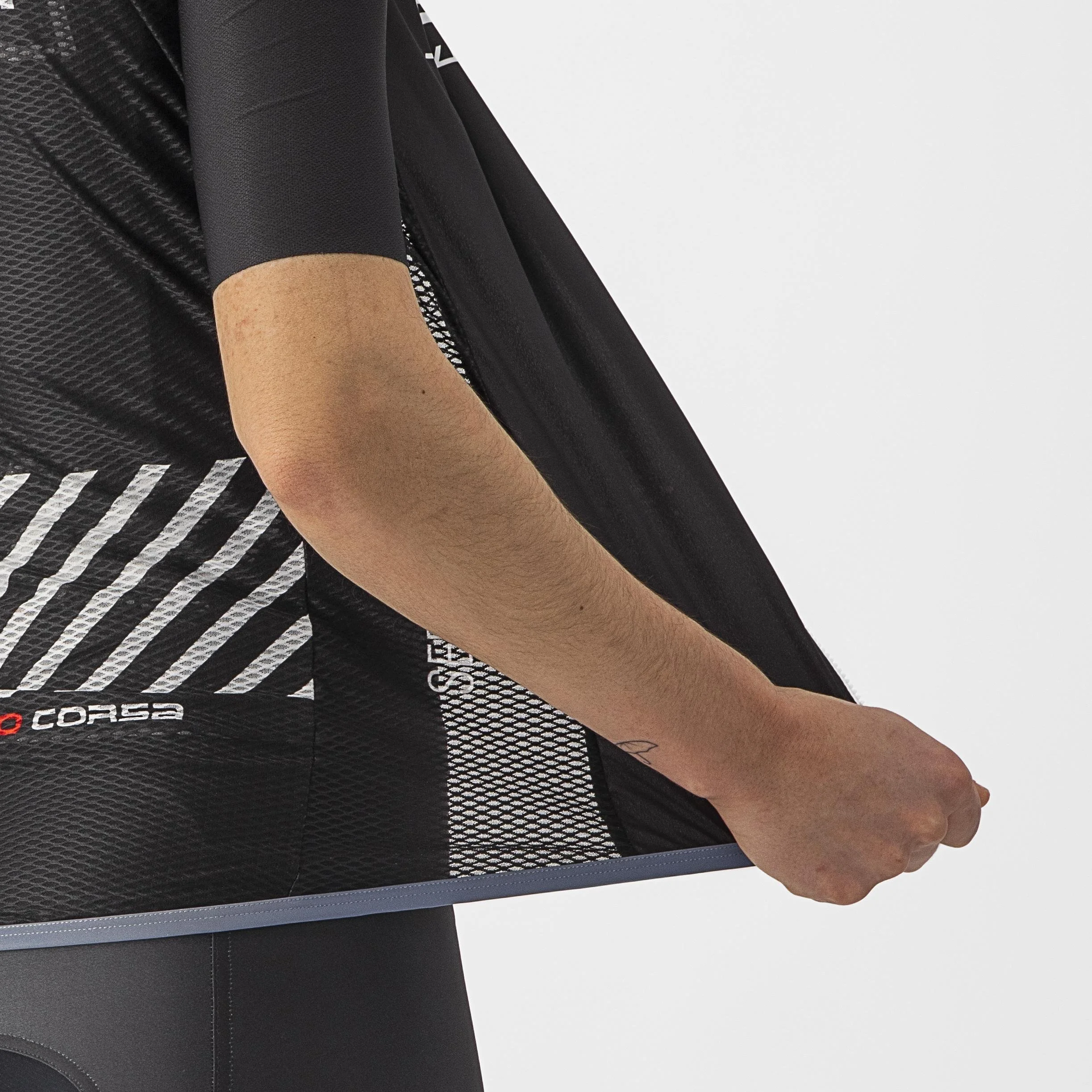Close-up van een persoon die een zwart sportshirt en bijpassende fietsbroek draagt, met de arm en hand zichtbaar die het shirt vasthoudt.