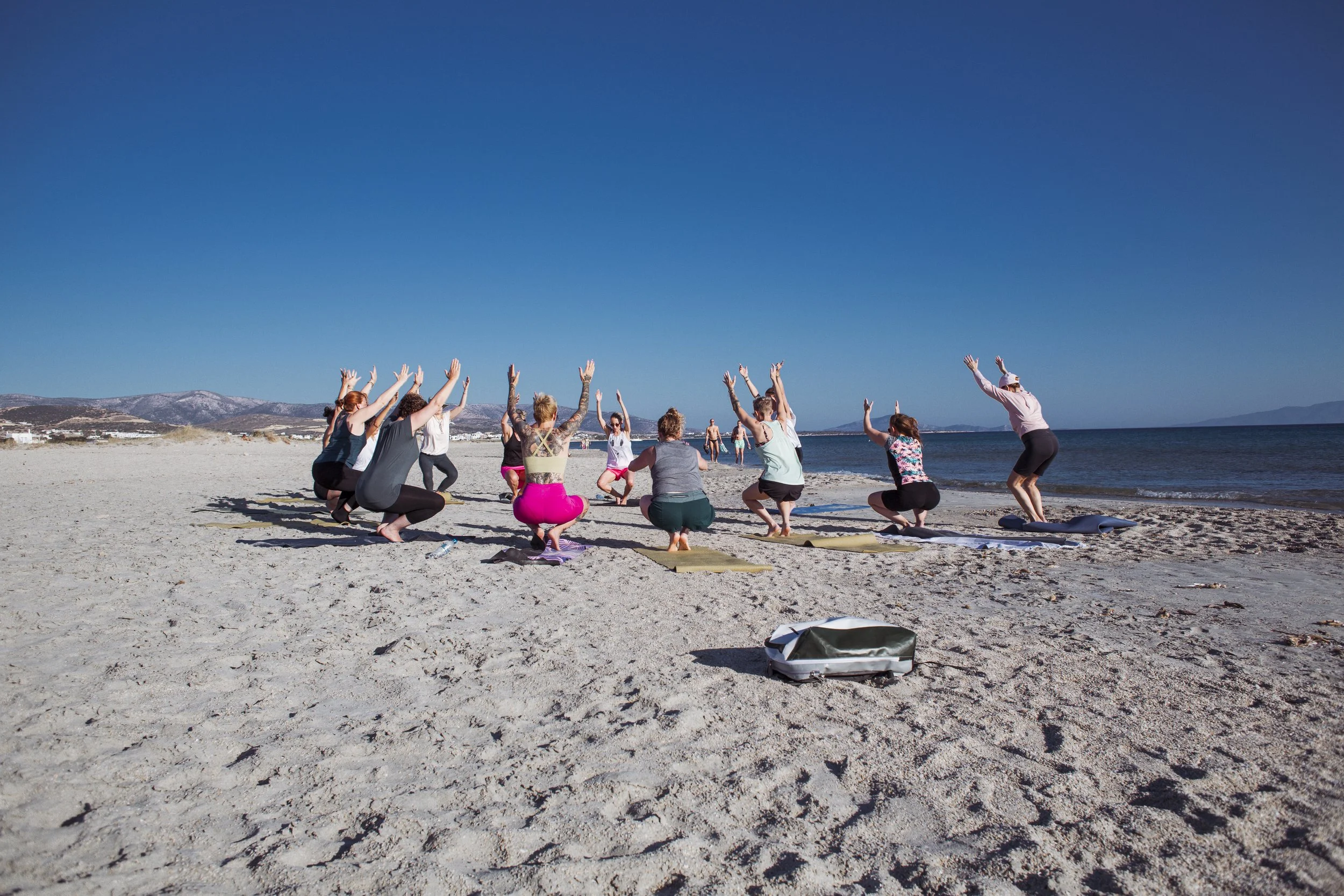 Menschen beim Strand-Yoga unter blauem Himmel, mit Meer im Hintergrund.