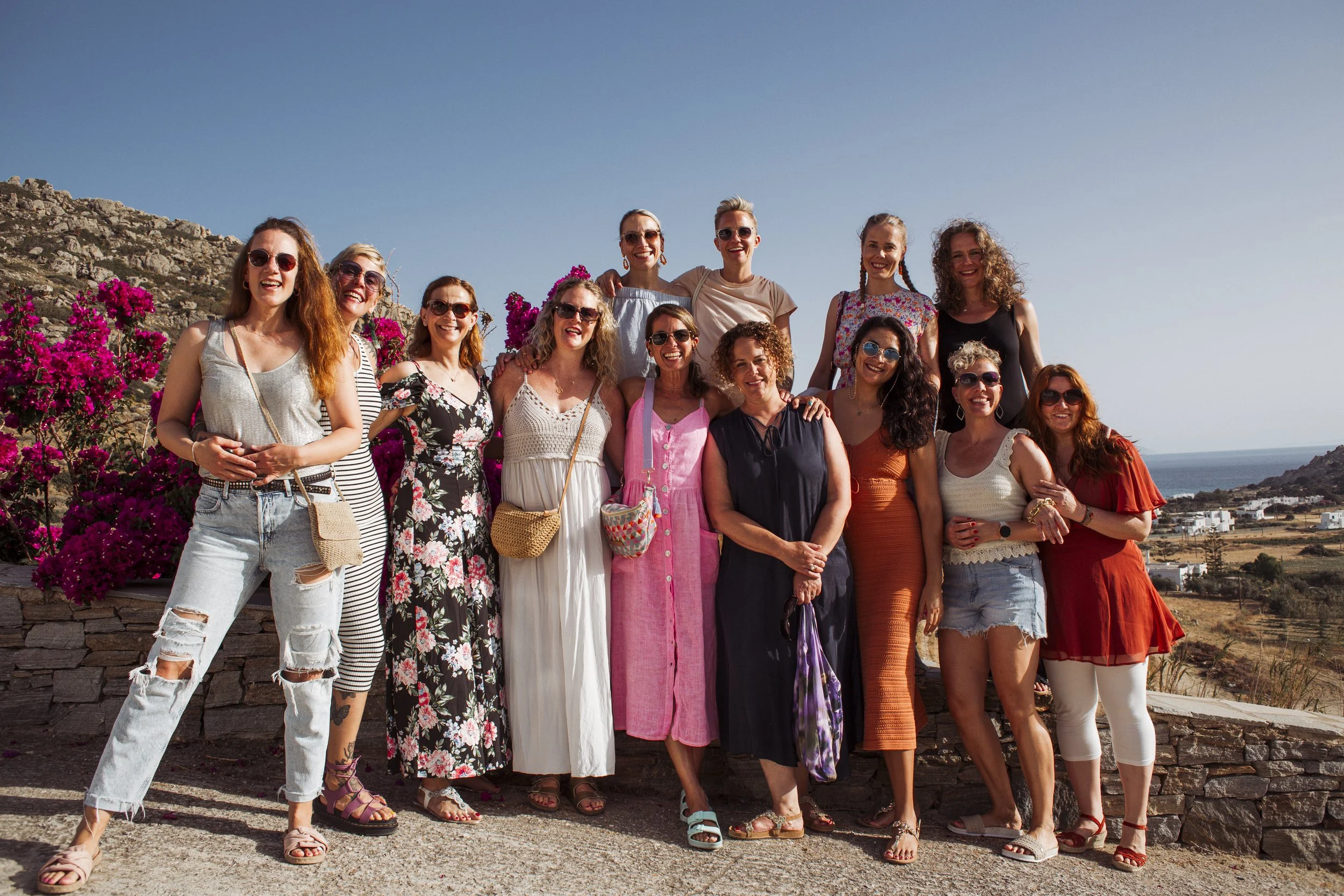 Gruppe von Frauen steht im Freien vor einer Landschaft mit Bergen und dem Meer, lächeln und posieren für das Foto an einem sonnigen Tag.