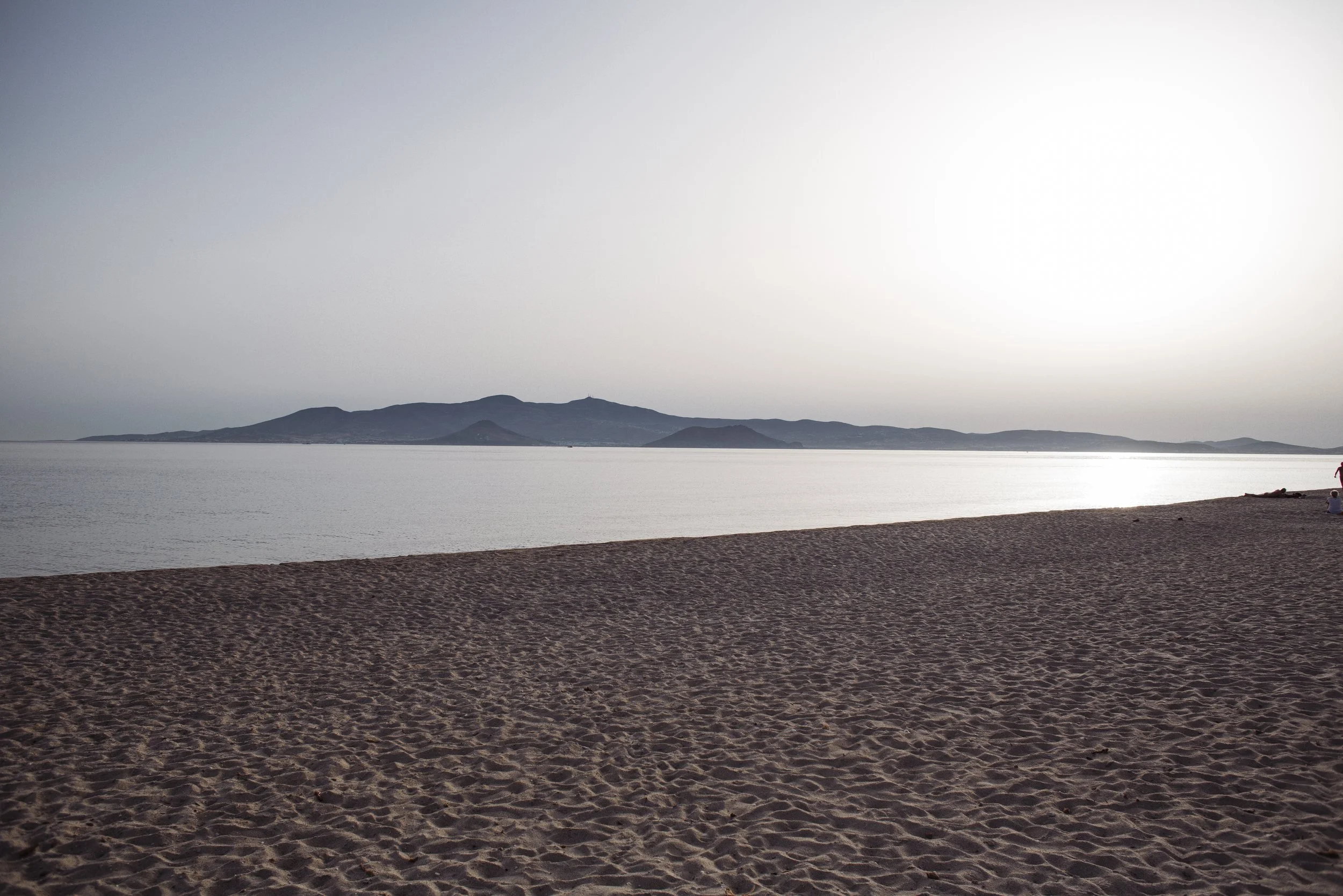 Ein ferner Berg mit einer leeren Sandstrand im Vordergrund bei Sonnenuntergang.