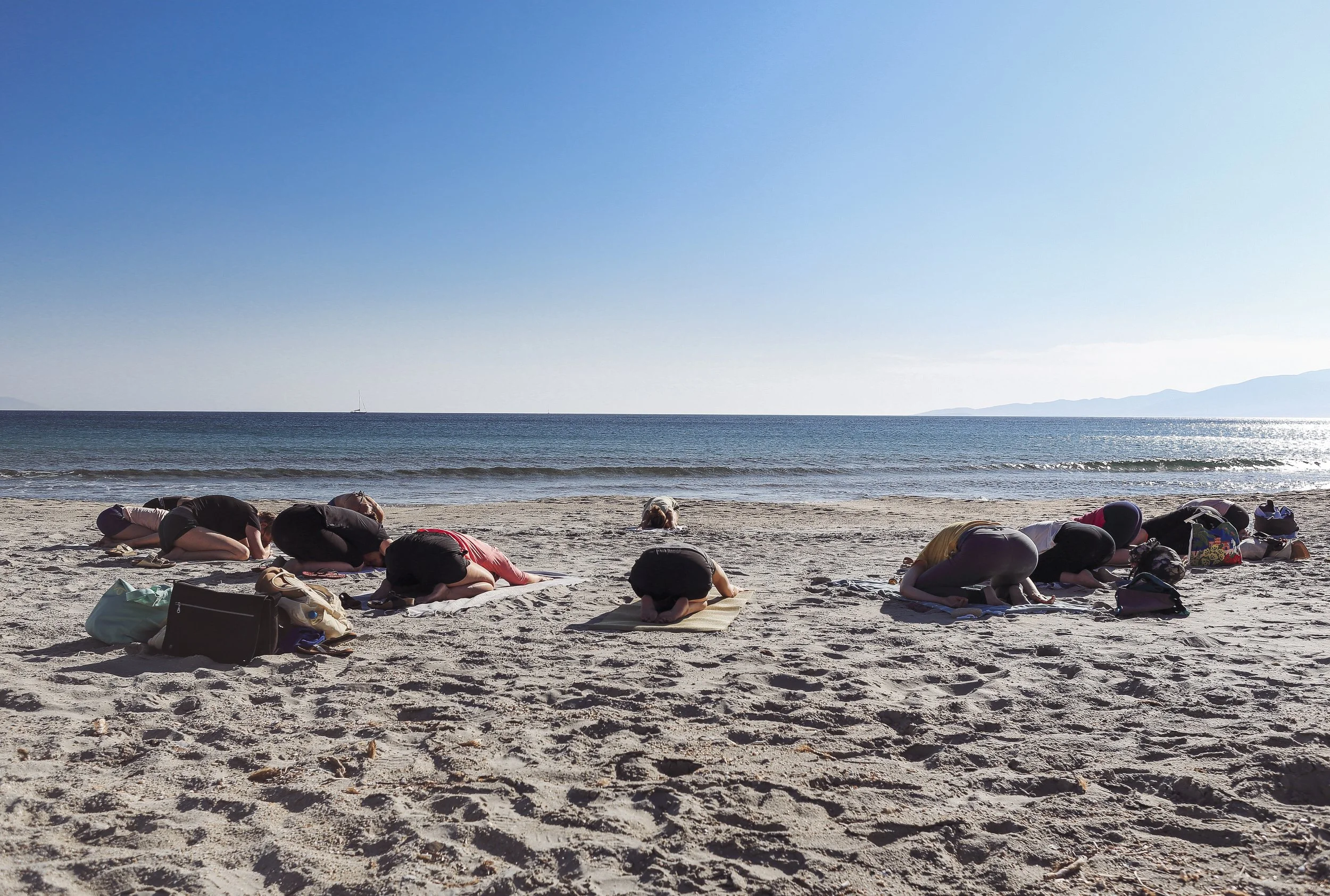 Menschen machen Yoga am Strand, sie sind in Kinderstellung, mit Blick auf das Meer und den Himmel.