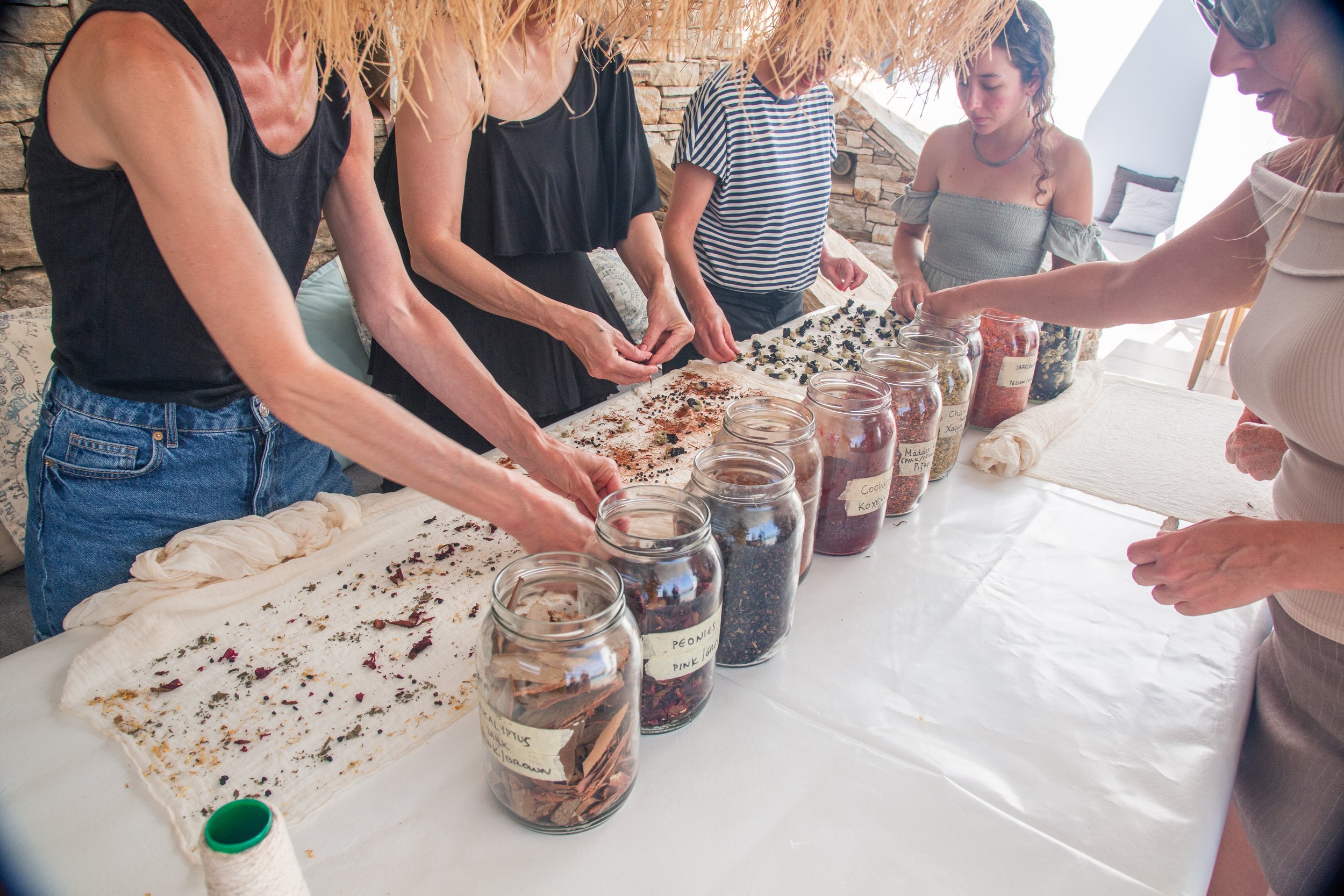 Mehrere Frauen arbeiten an der Herstellung von Kräutertees, indem sie getrocknete Kräuter aus Gläsern auf ein Tuch streuen.