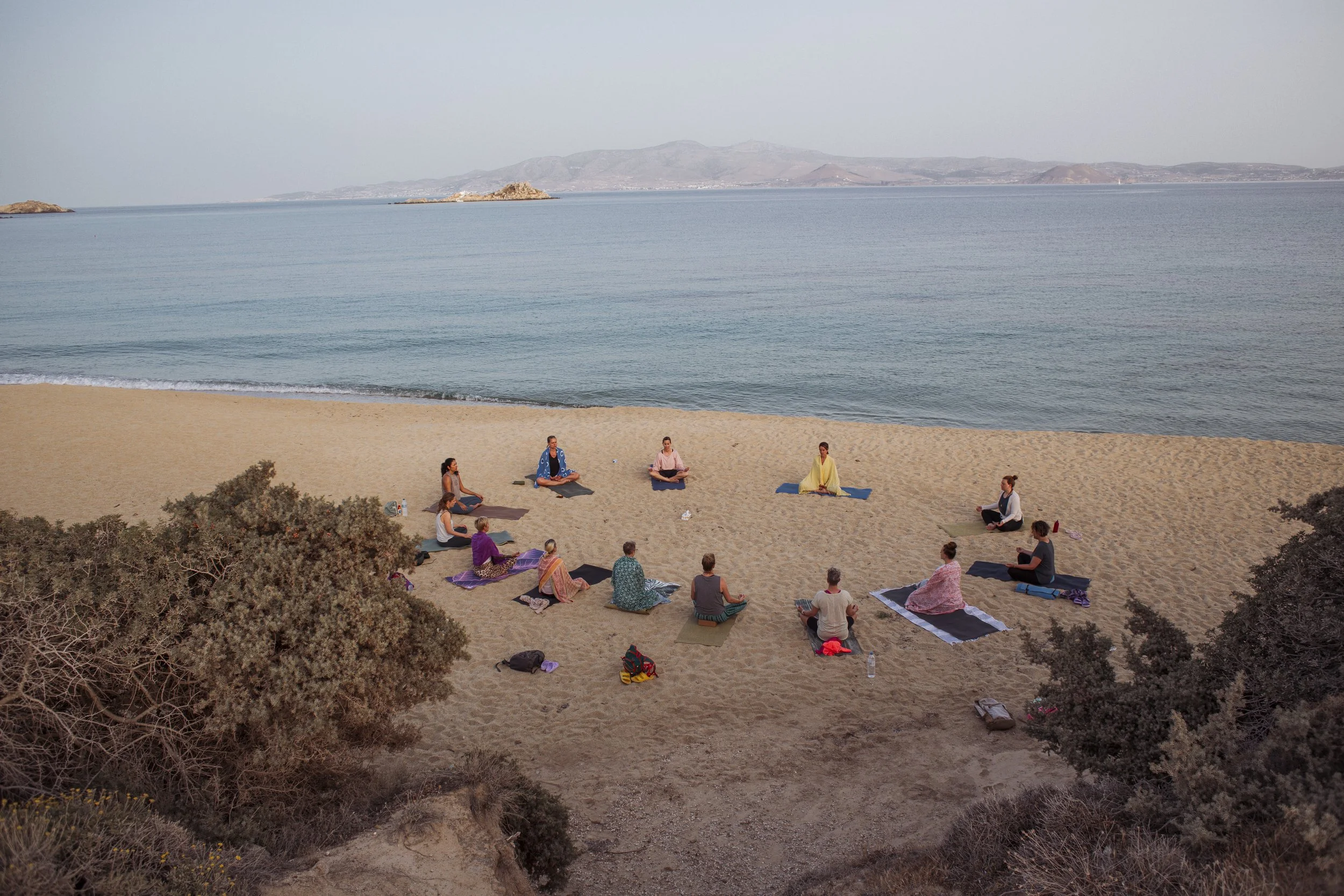 Menschen beim Yoga am Strand mit Blick auf das Meer bei Sonnenuntergang.
