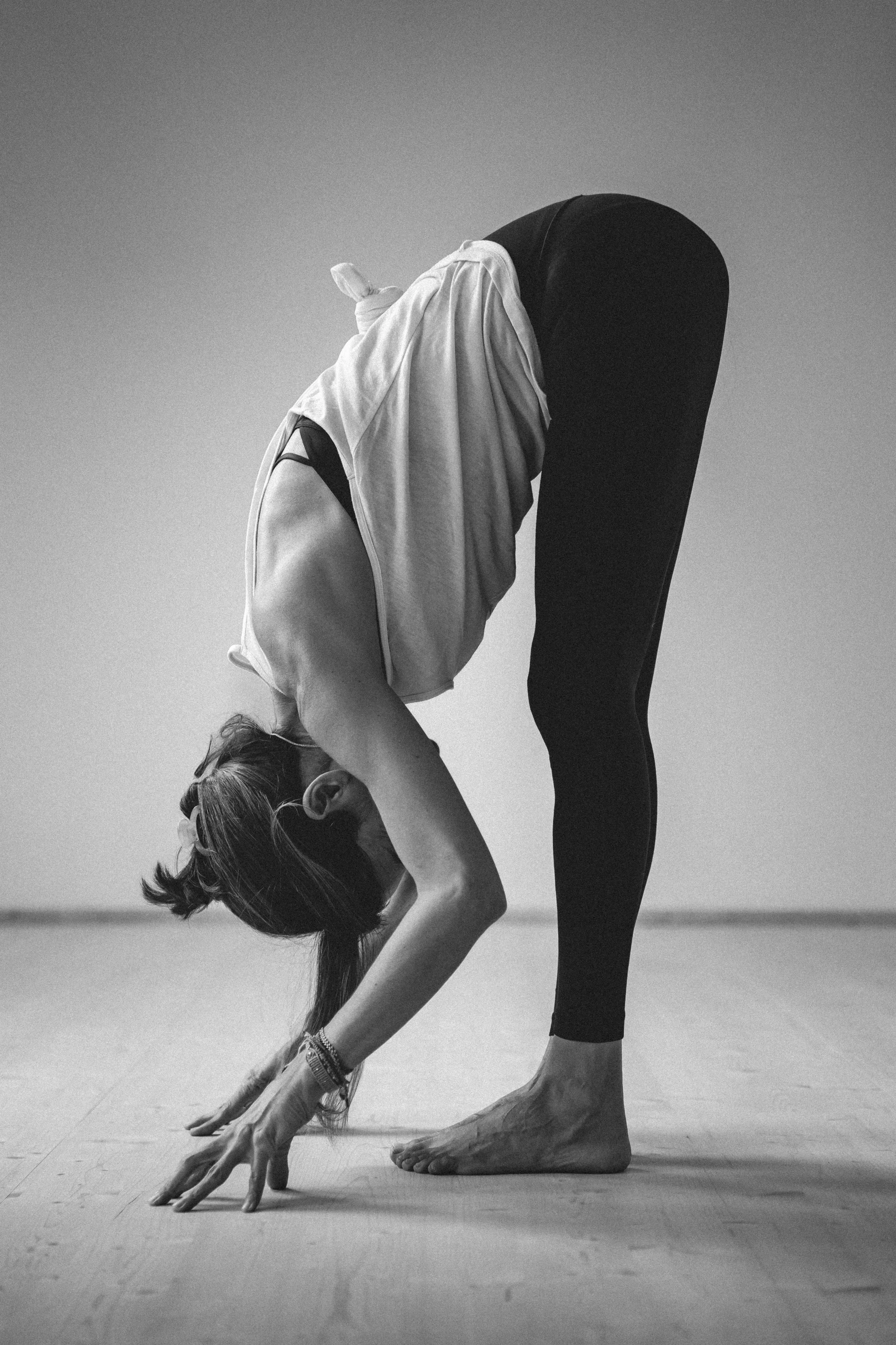 Frau in Yoga-Position, die nach vorne gebeugt ist, auf glattem Boden in einem Raum