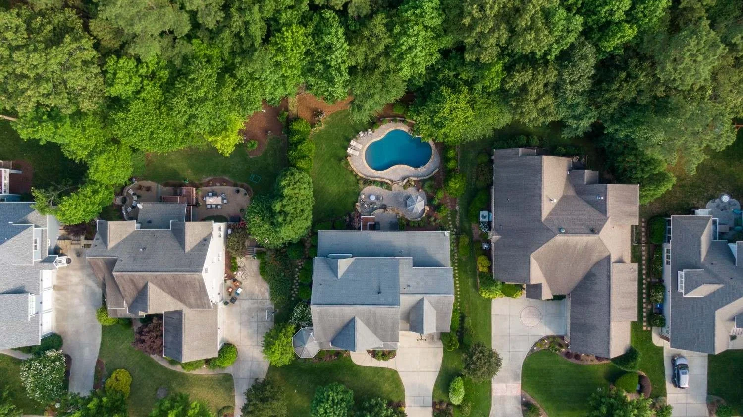 Aerial view of a suburban neighborhood featuring residential homes, green trees, and landscaped properties.