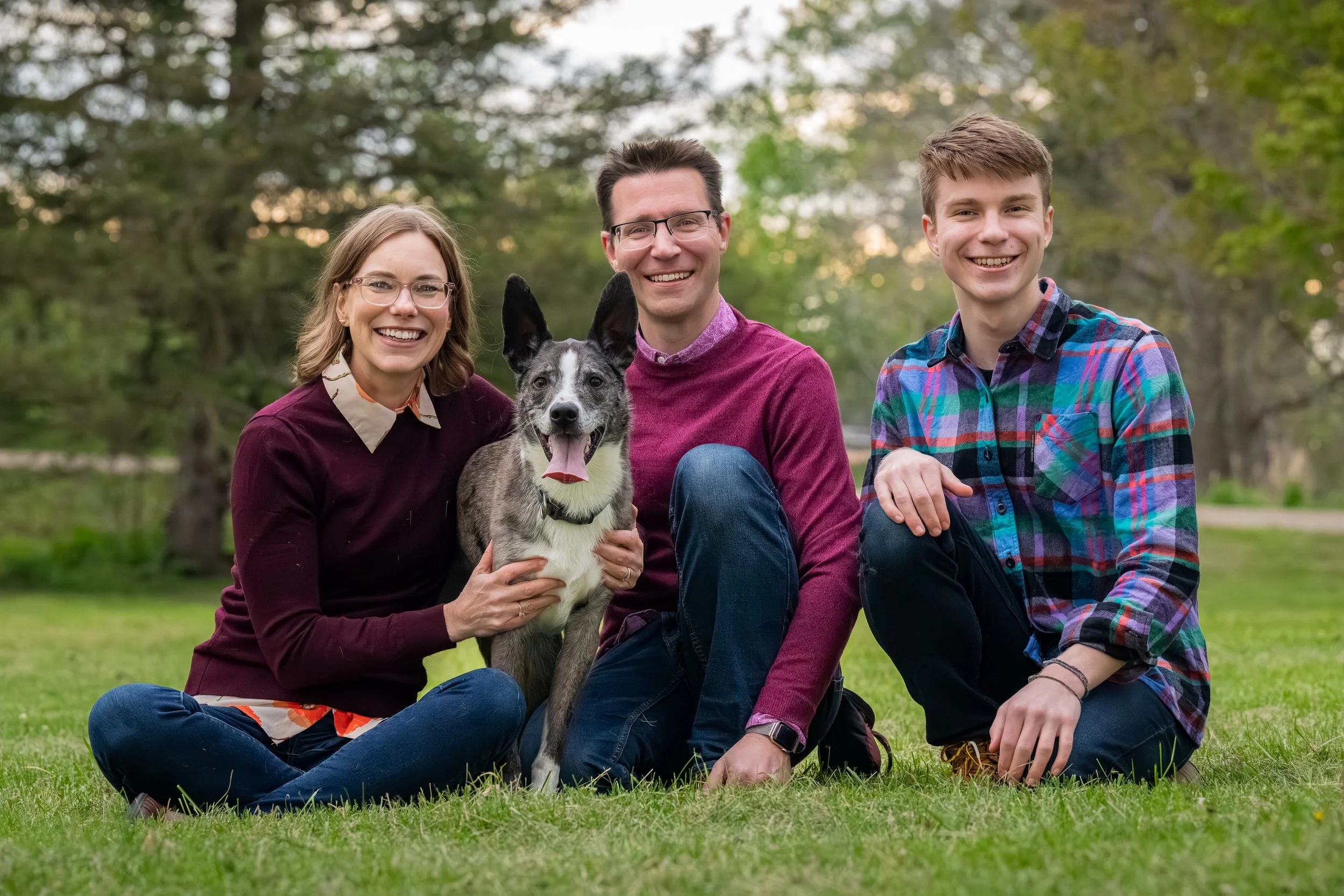 Black and gray dog with family wearing purple and plum tones during outdoor pet portrait session, Southeast Michigan.