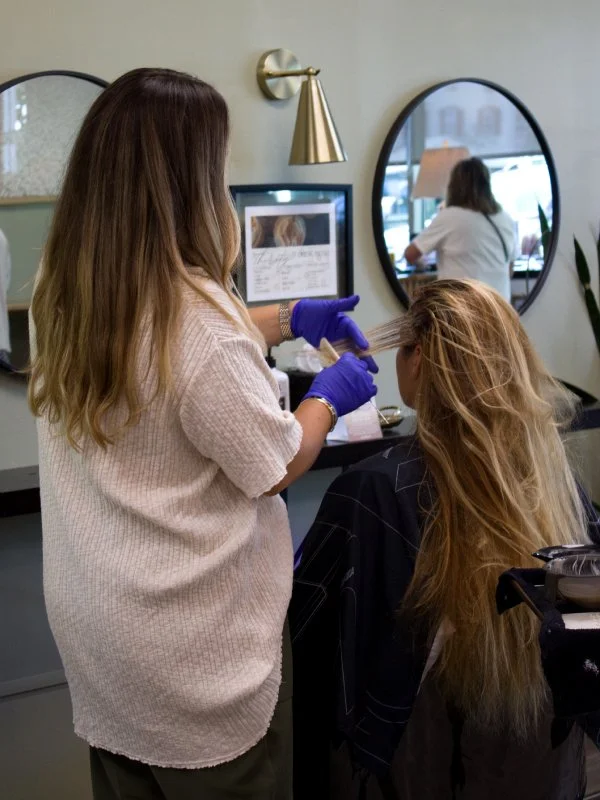 Hair stylist coloring clients hair in salon.