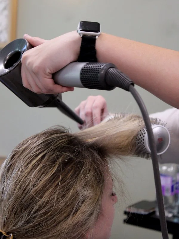 Close up of hair stylist blow drying hair with brush.