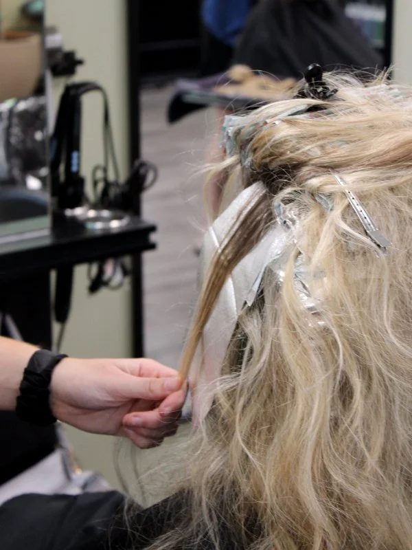 Hair stylist working on client coloring blonde hair at the roots.