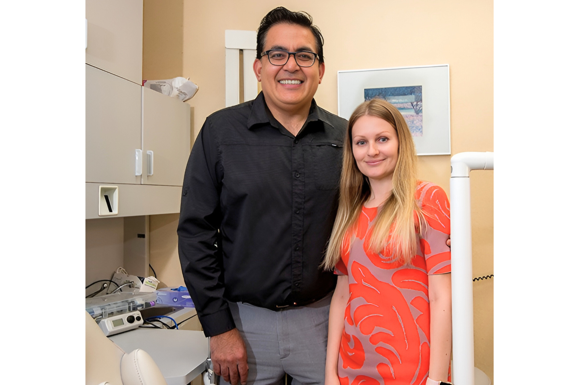 A man and woman standing side by side inside a medical office or clinic, smiling at the camera.