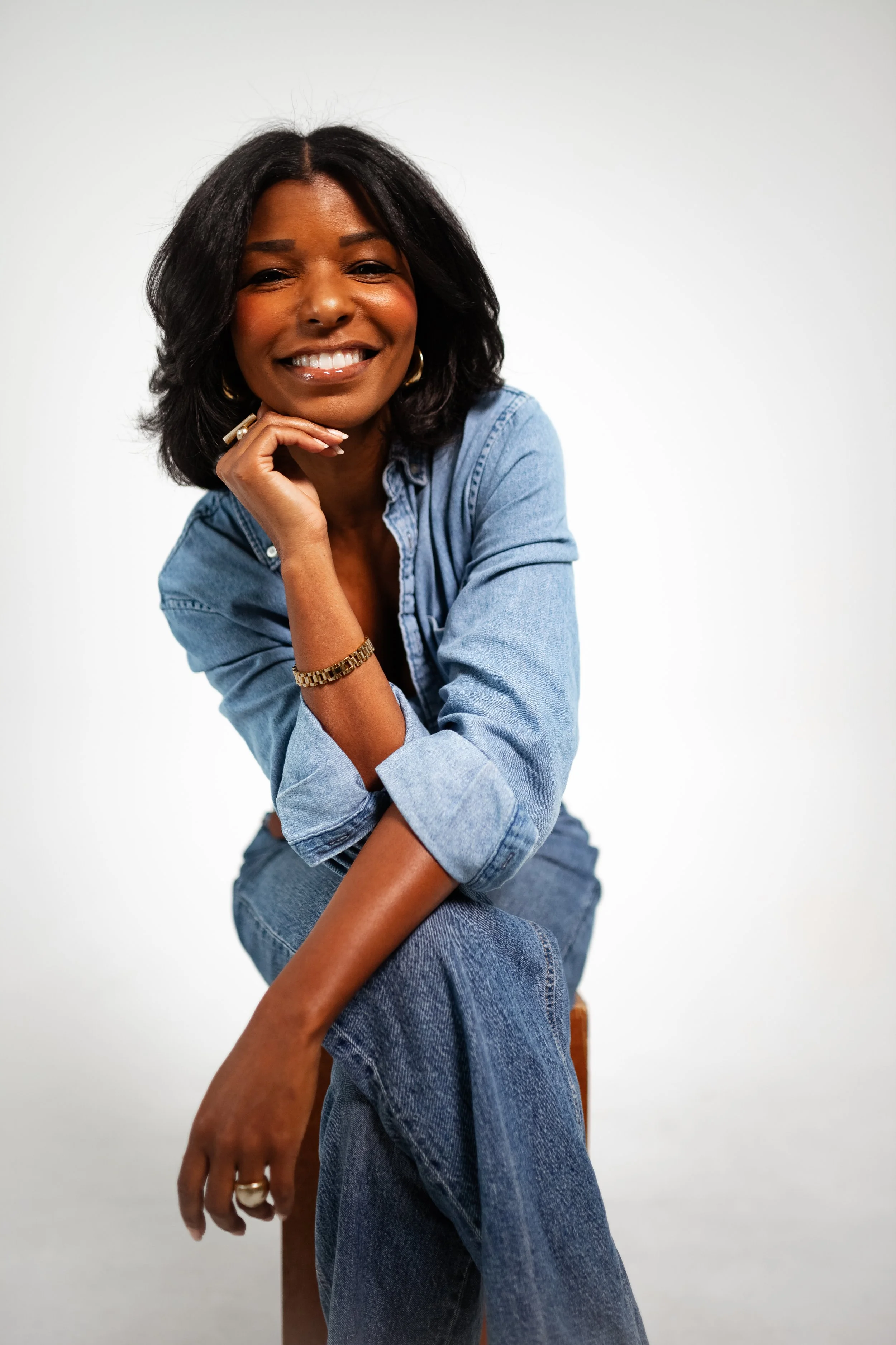 Studio portrait of Dr. Kimberly McGlonn smiling while seated in a denim shirt and jeans