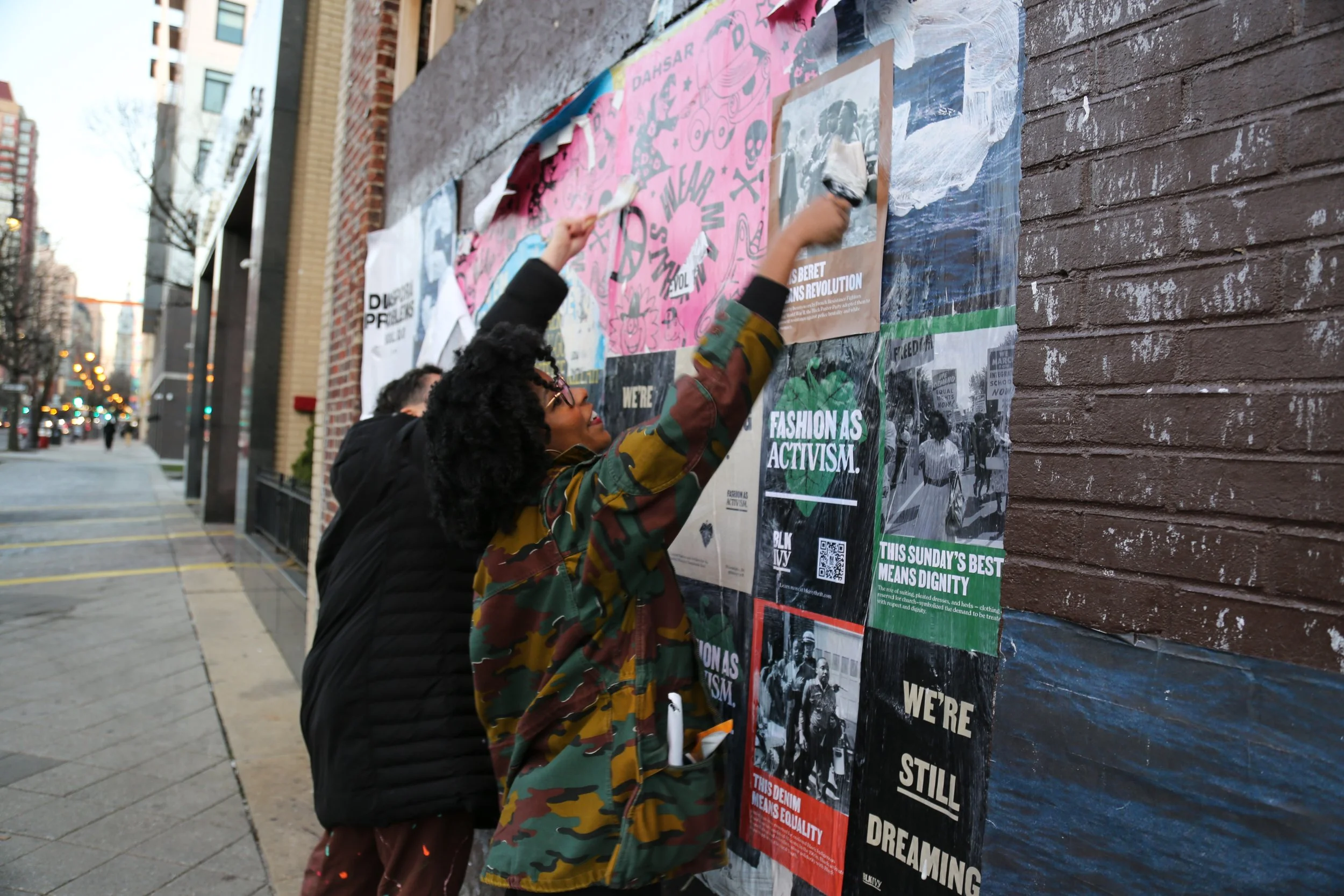 People putting up Fashion as Activism posters on a city wall