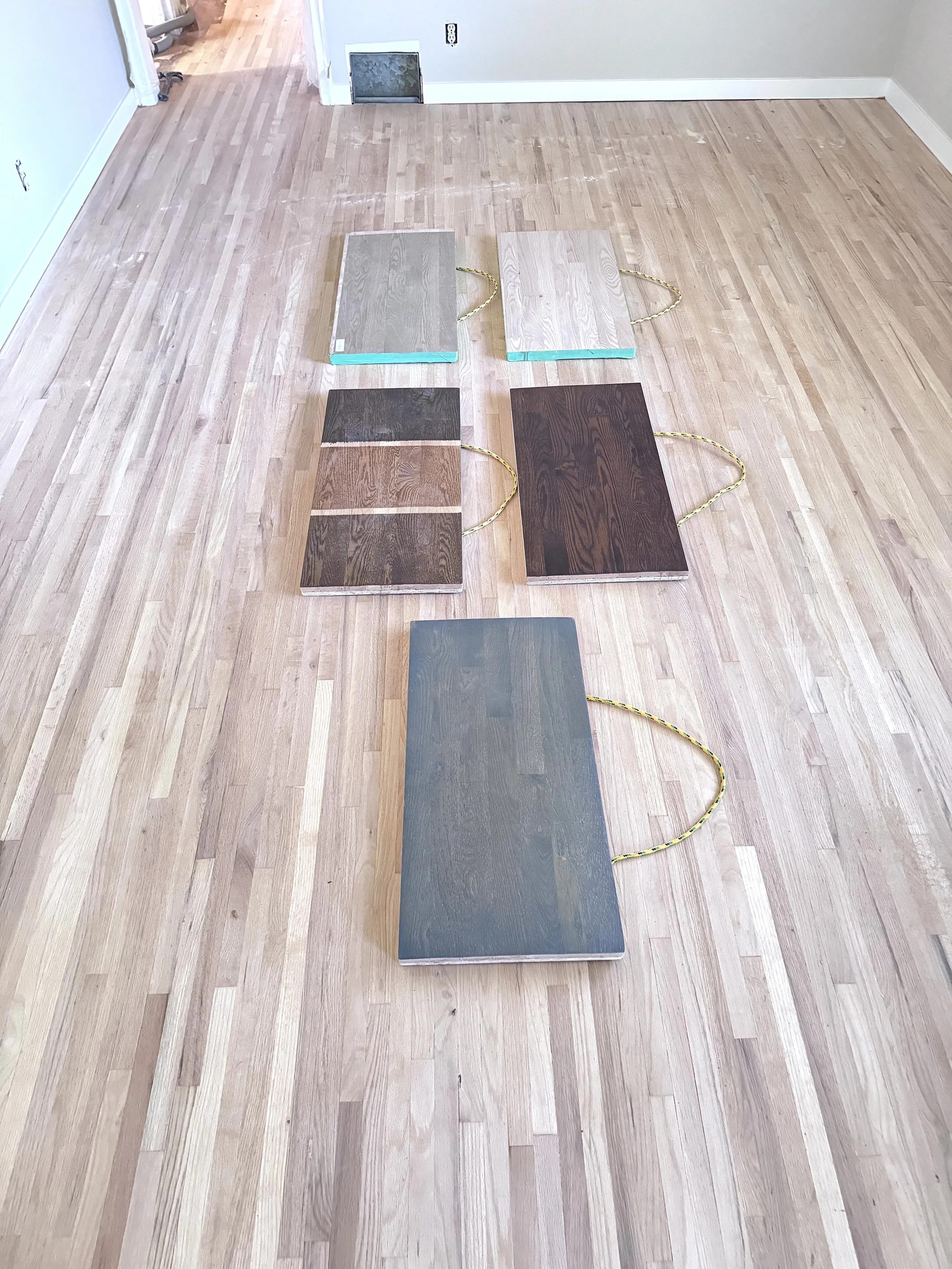5 different stain color samples laying on a bare wood floor