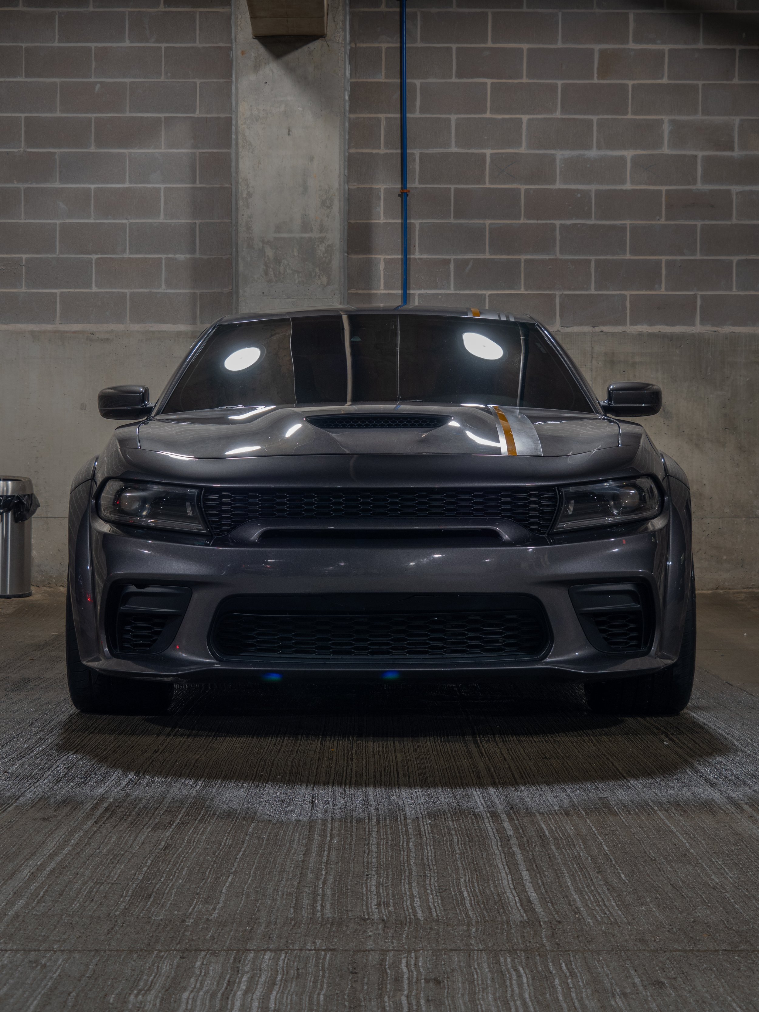 Front view of a gray sports car with racing stripes in a dimly lit parking garage.