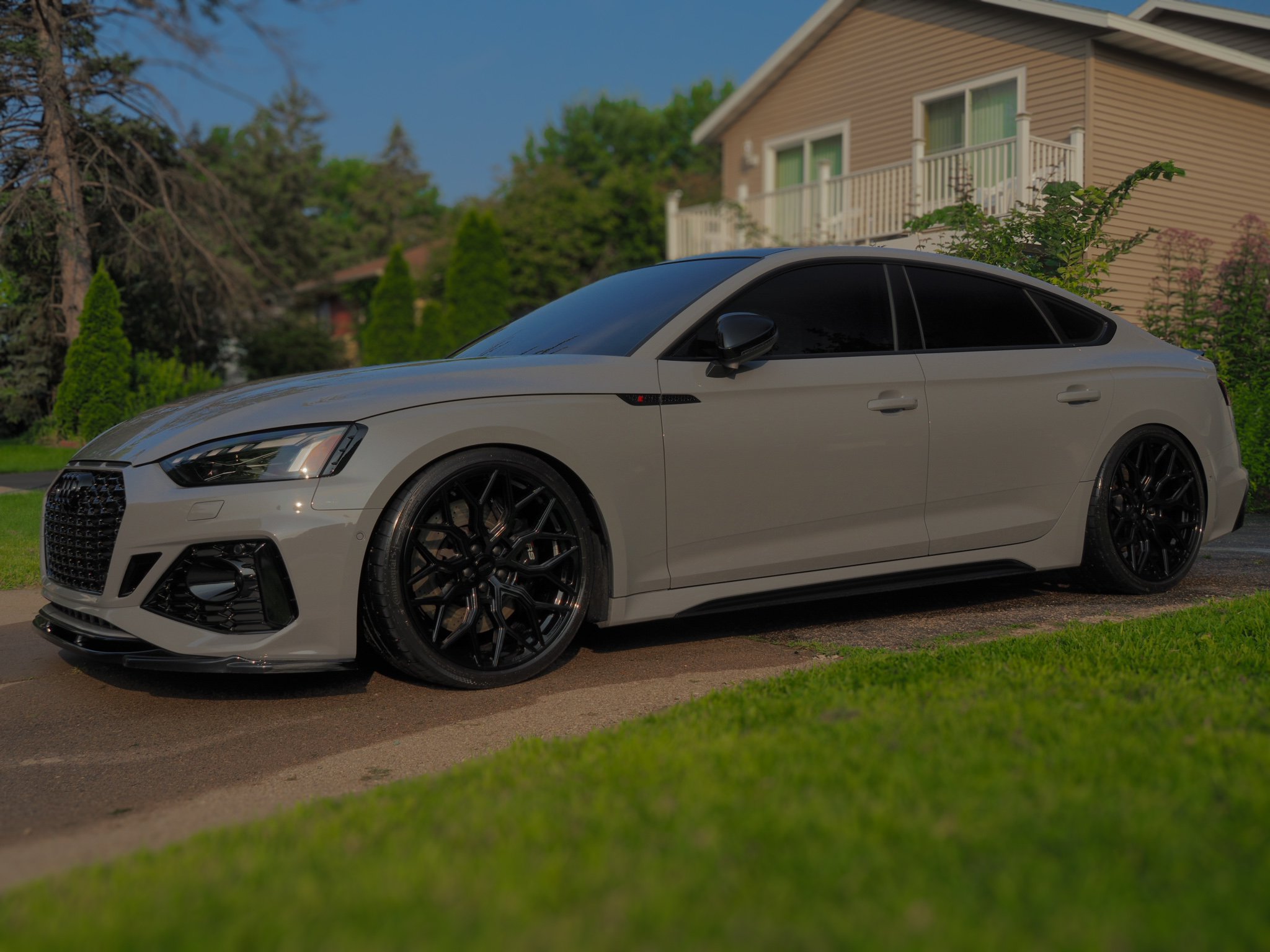White luxury sedan parked outside a residential home with a manicured lawn and trees in the background.