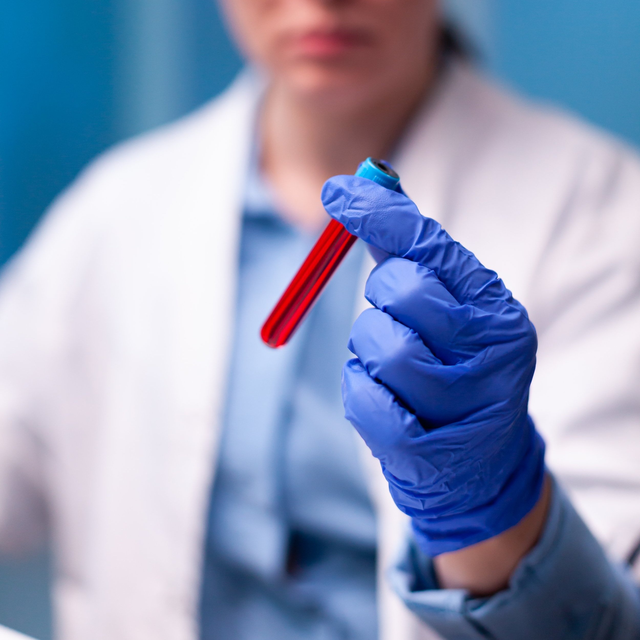 Un científico con guantes azules sosteniendo una muestra de sangre en un tubo de ensayo.