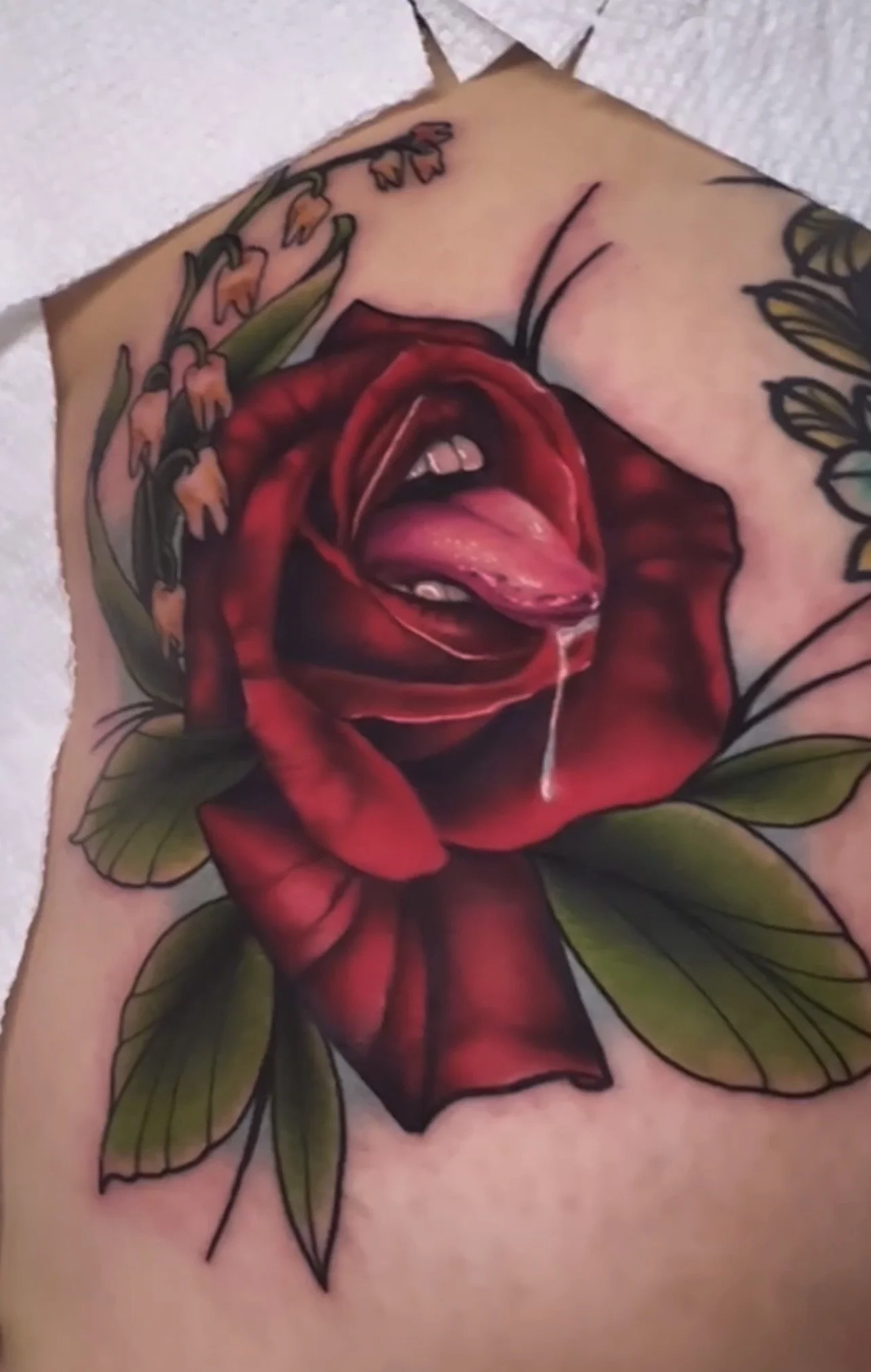 Tattoo of a realistic open red rose with green leaves on someone's skin.
