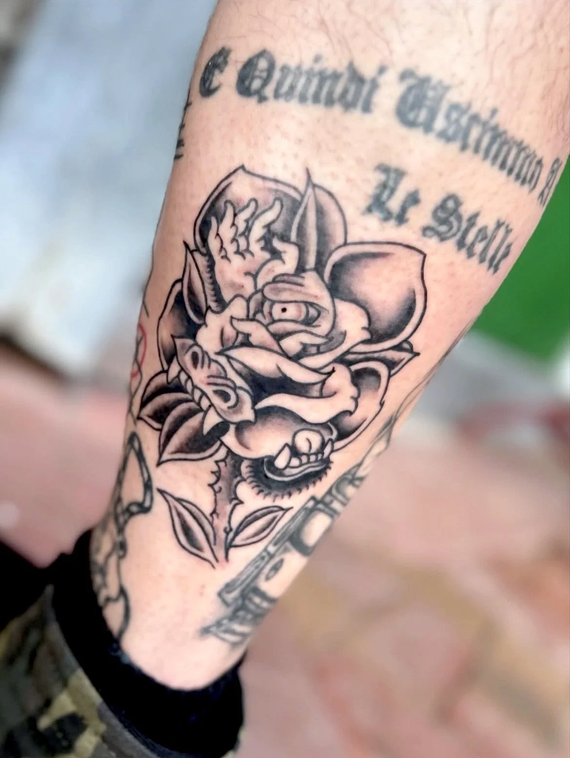 Tattoo on person's arm featuring a dragon intertwined with a rose, with a banner above that reads 'C railor G' and the number '14' visible, along with other text partially shown.