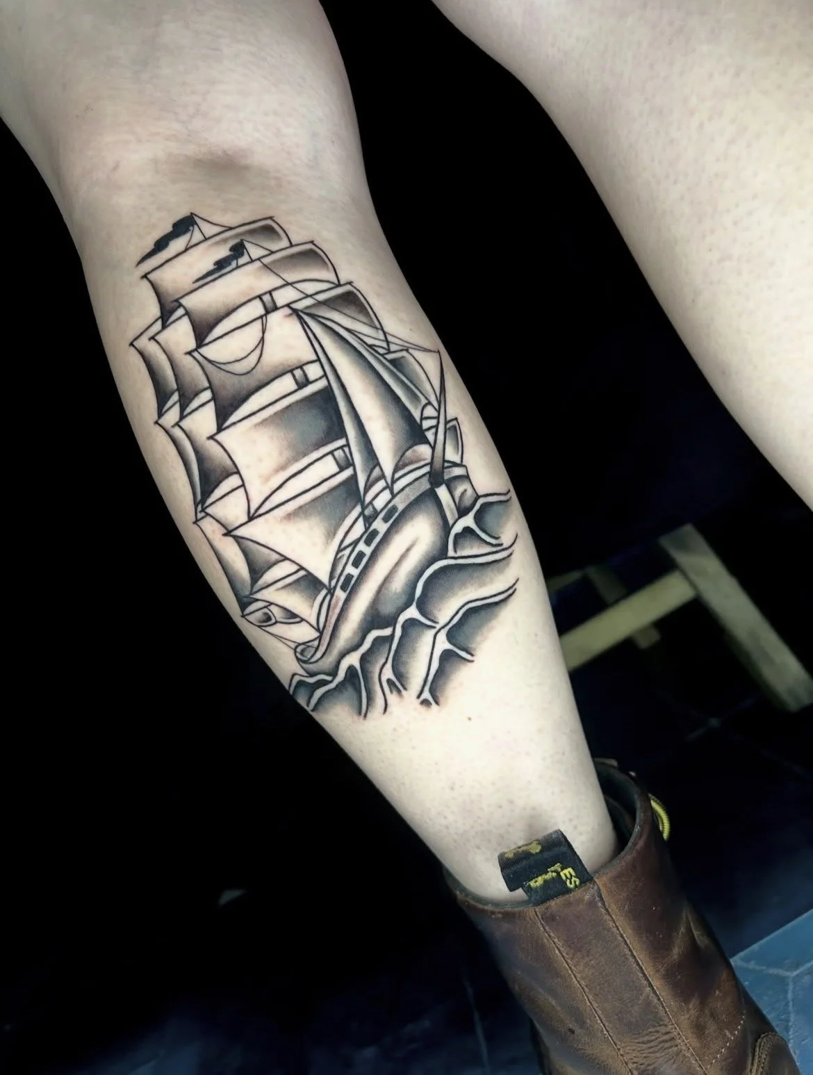 Black and gray tattoo of a sailing ship with sails, rigging, and waves on a person's forearm.