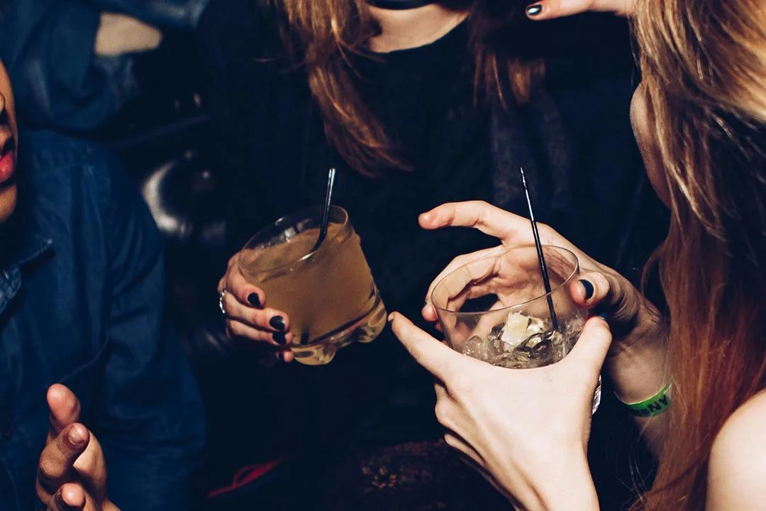 People holding drinks with ice in a dimly lit setting, possibly a bar or club.
