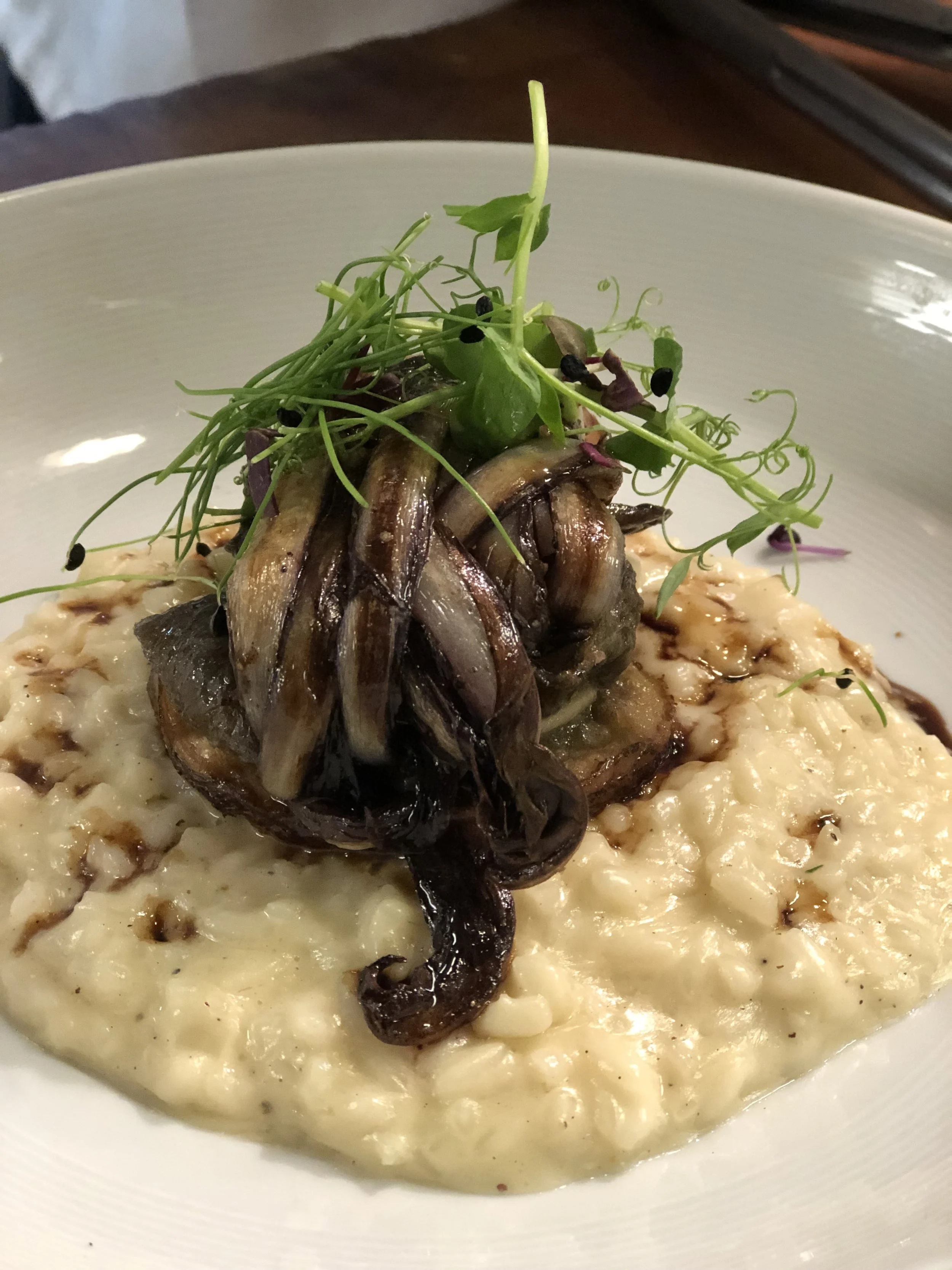 Creamy risotto topped with sautéed wild mushrooms and microgreens garnished with balsamic reduction.