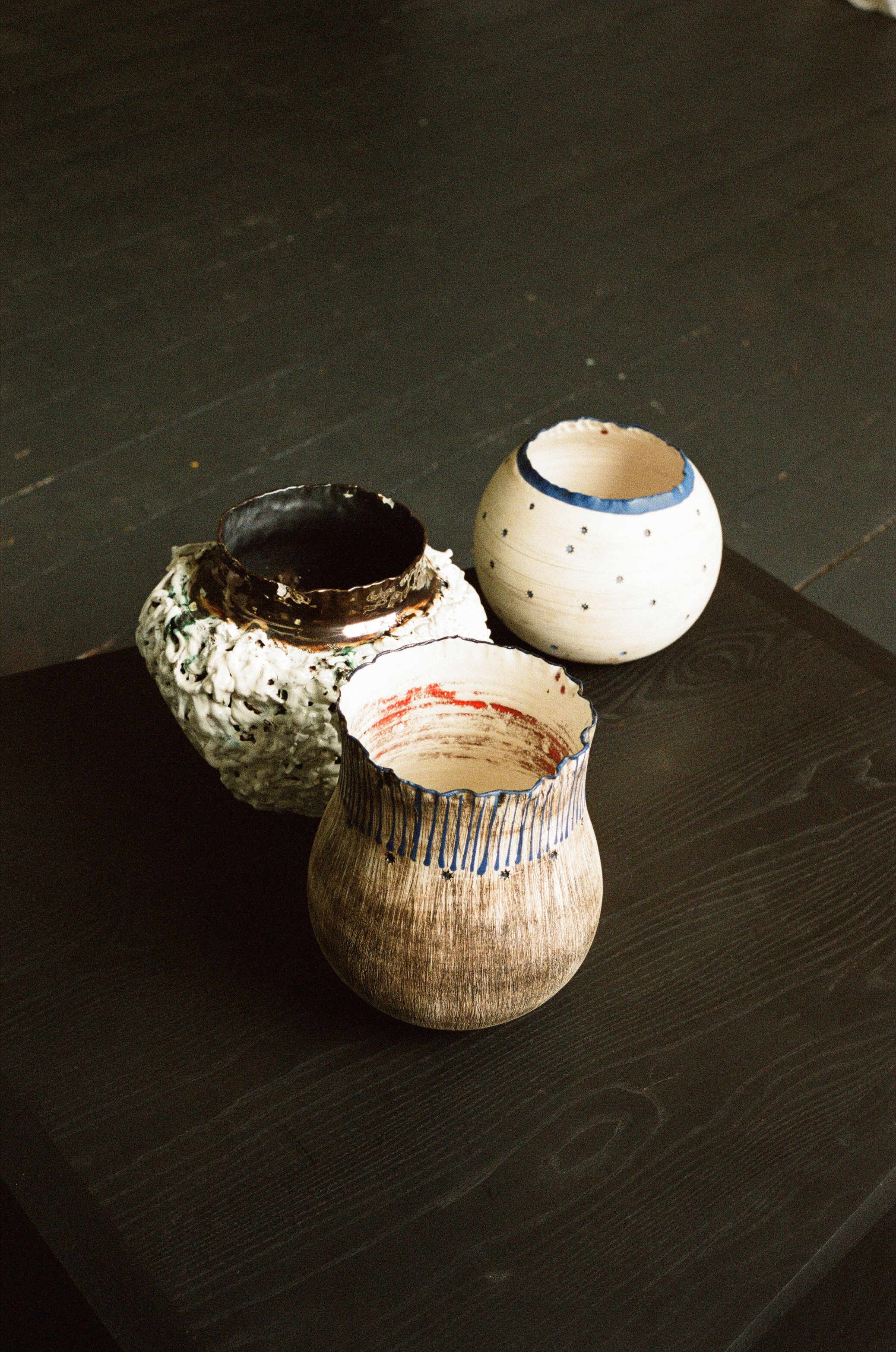 Three handmade ceramic vases on a dark wooden surface, each with unique textures and designs.