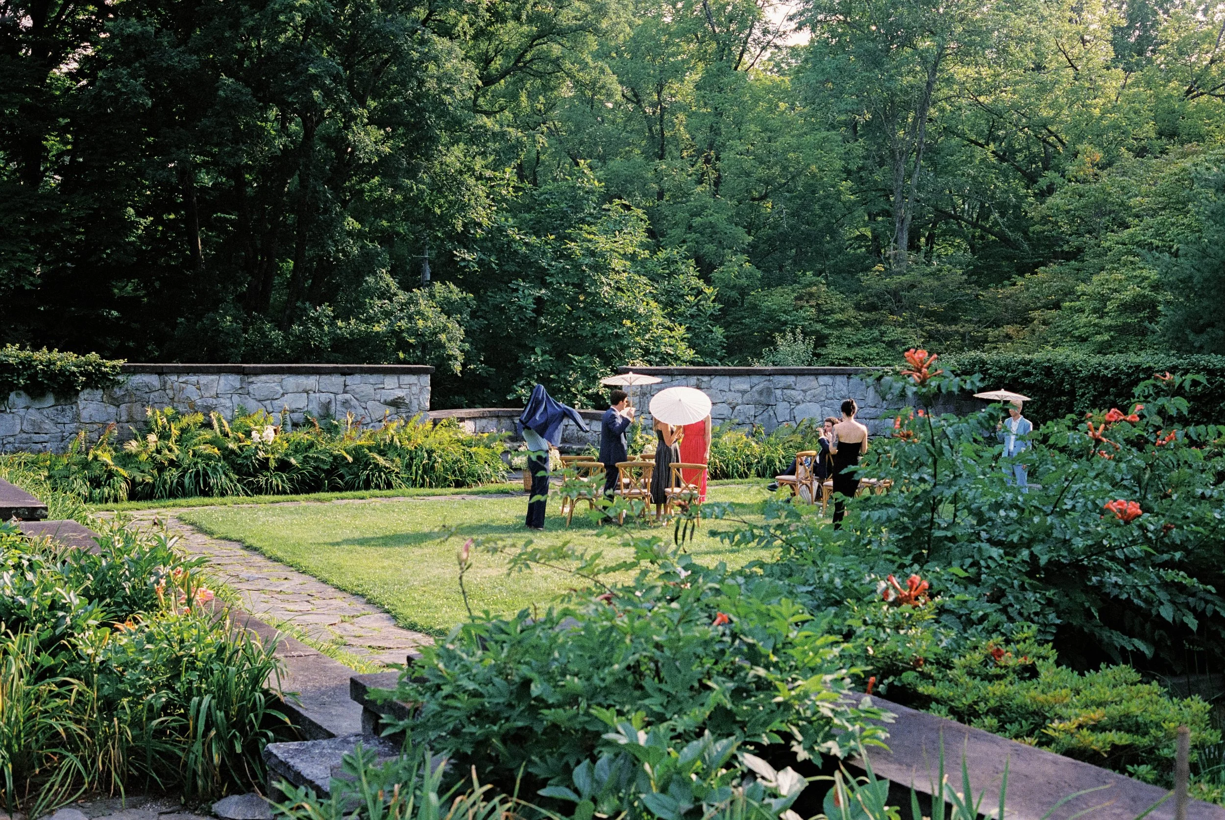 A color film photograph of wedding guests in a garden before the ceremony at Troutbeck in Amenia, New York