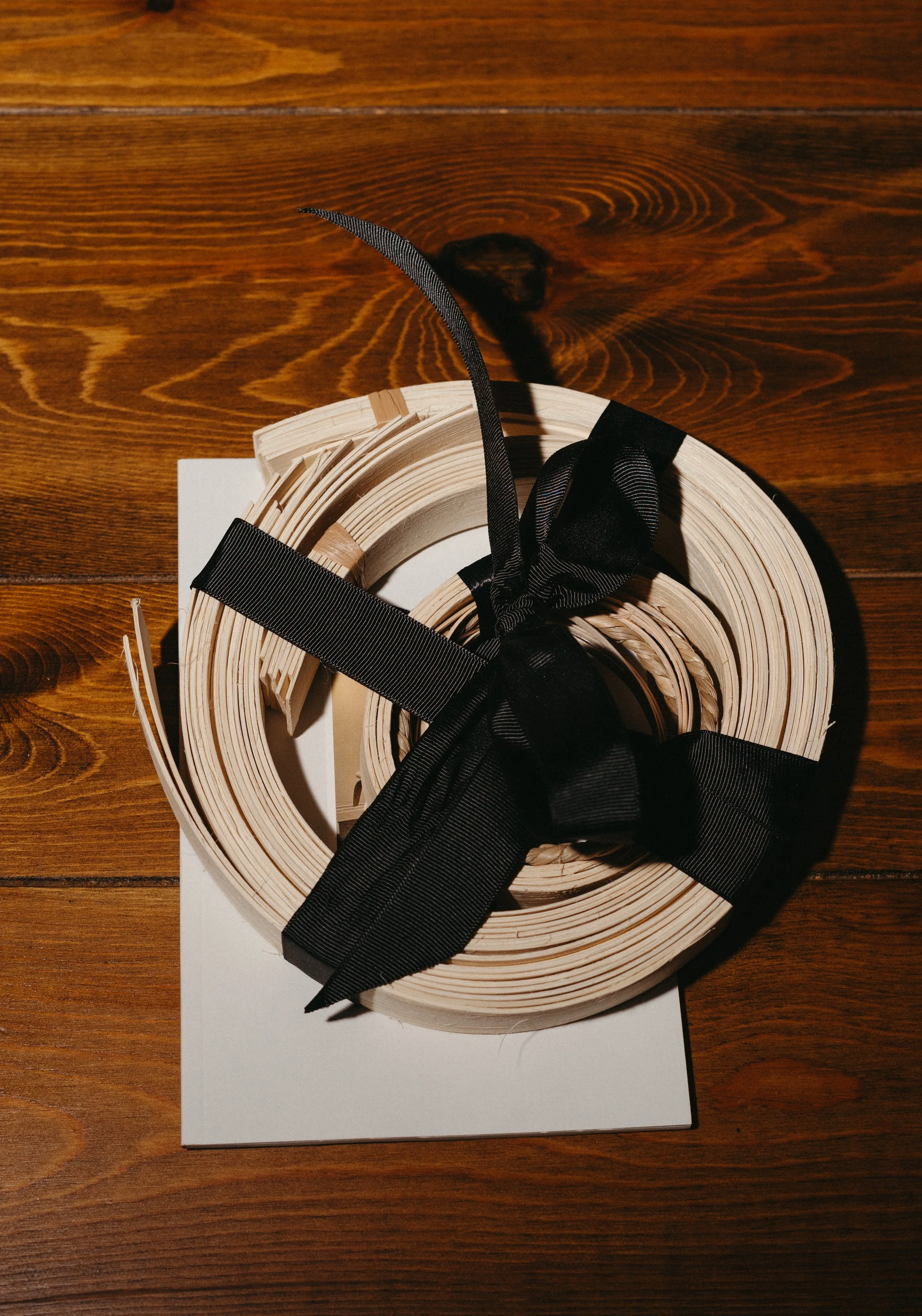 A spooled roll of white paper or ribbon tied with a black ribbon, placed on a white box on a wooden surface.