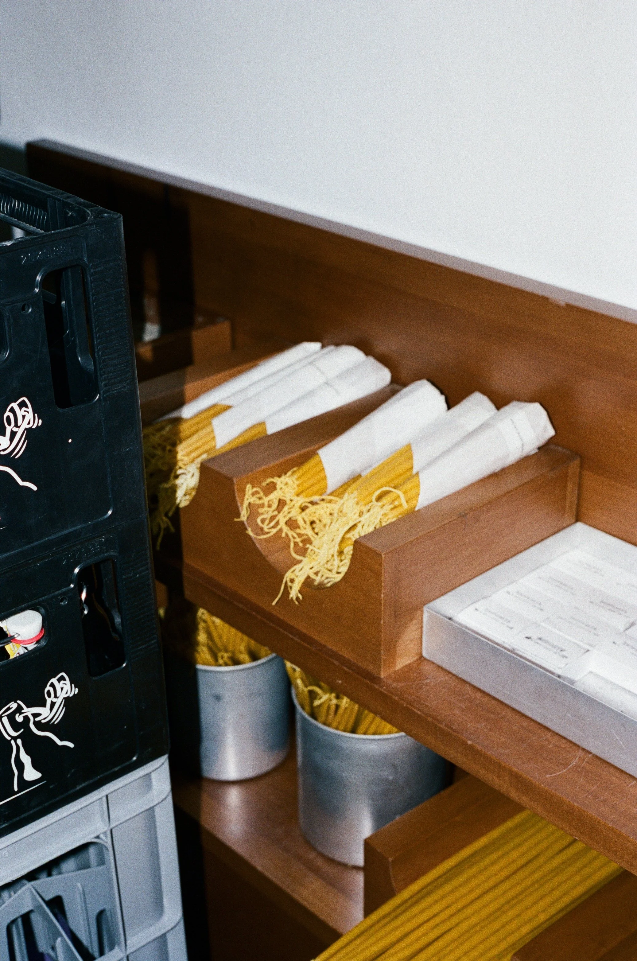 Boxes of uncooked spaghetti pasta on a wooden shelf in a kitchen or pantry.