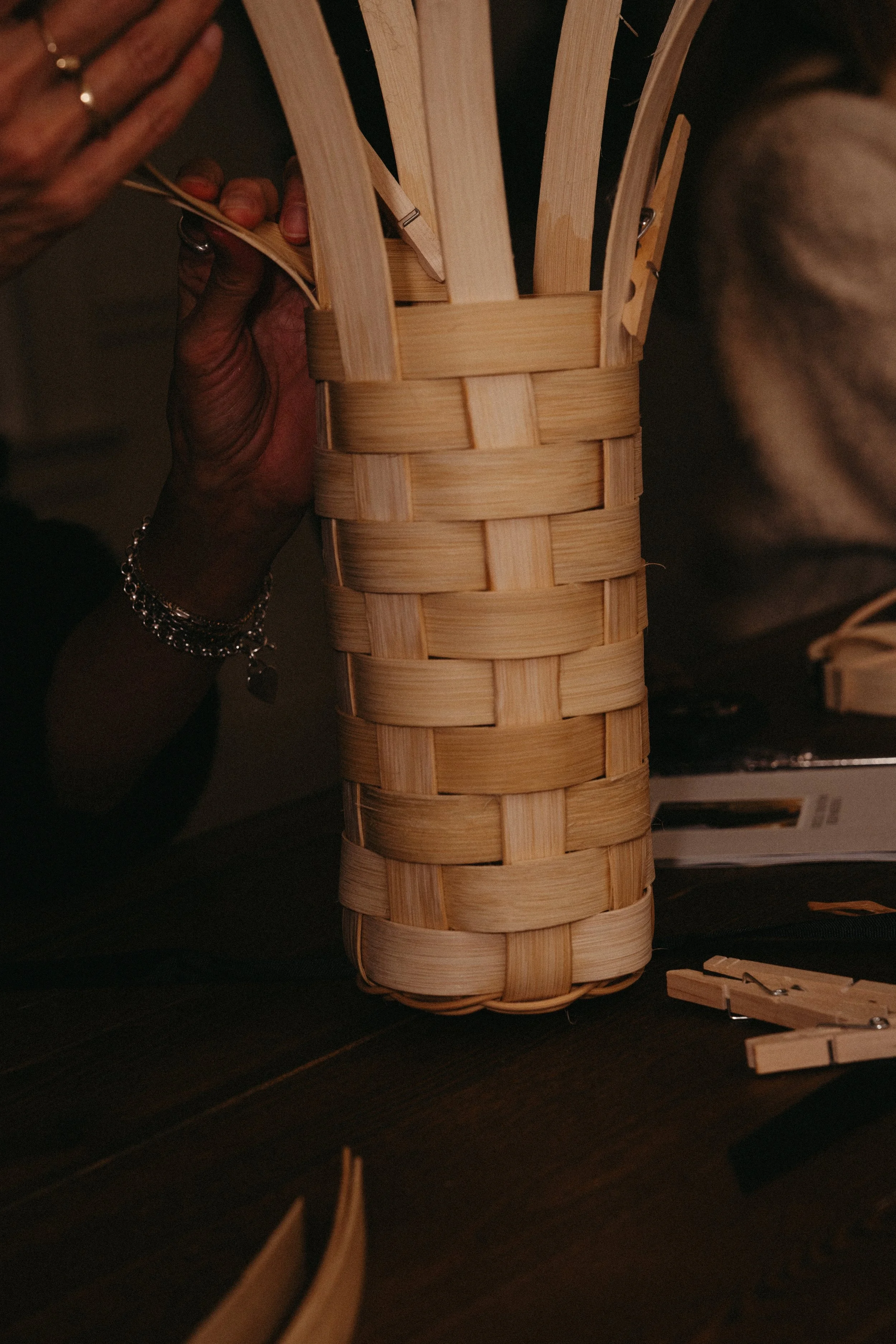 A person weaving a small basket with wooden strips.