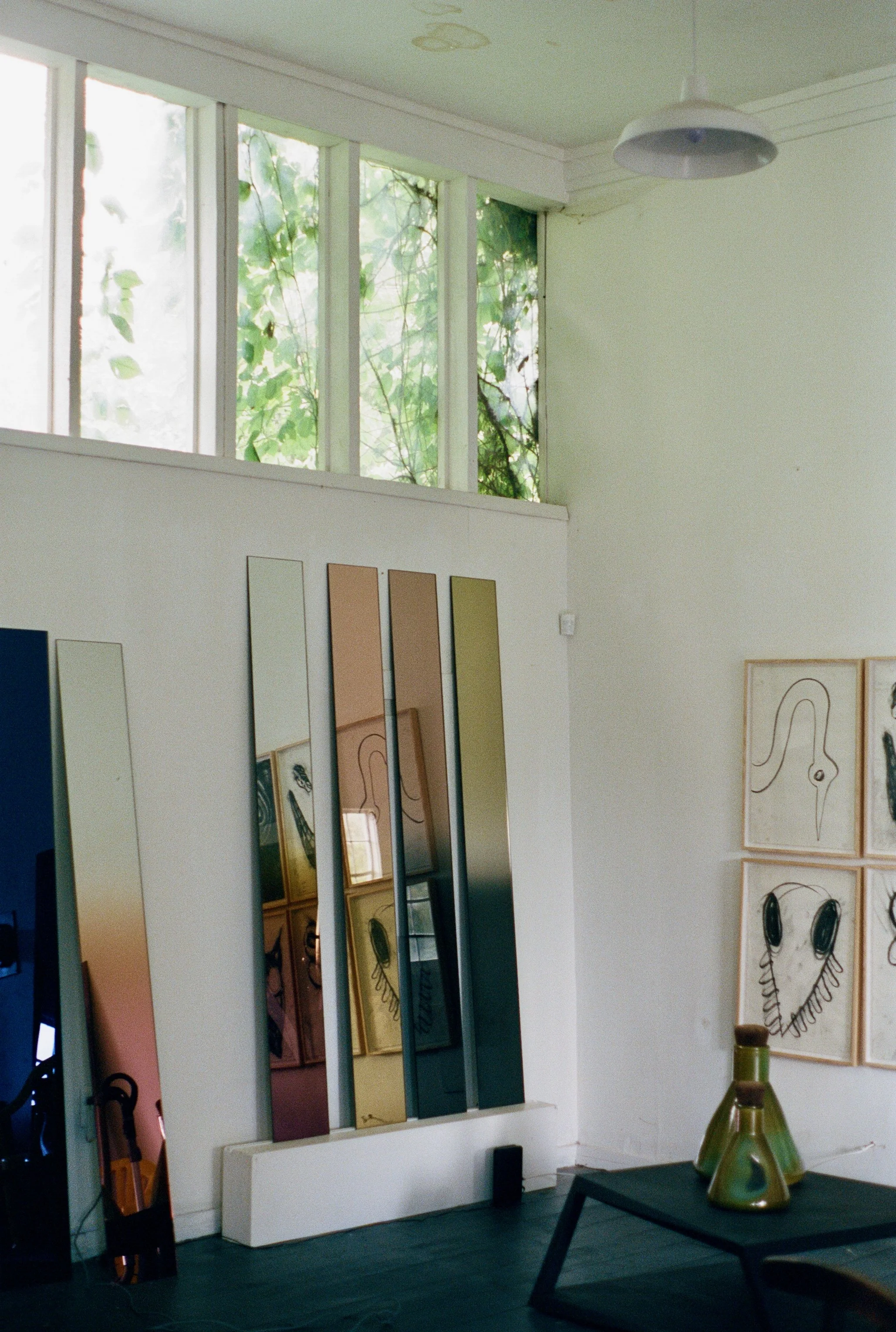 Interior of an art gallery with mirrors, framed artwork, and decorative vases on a table.