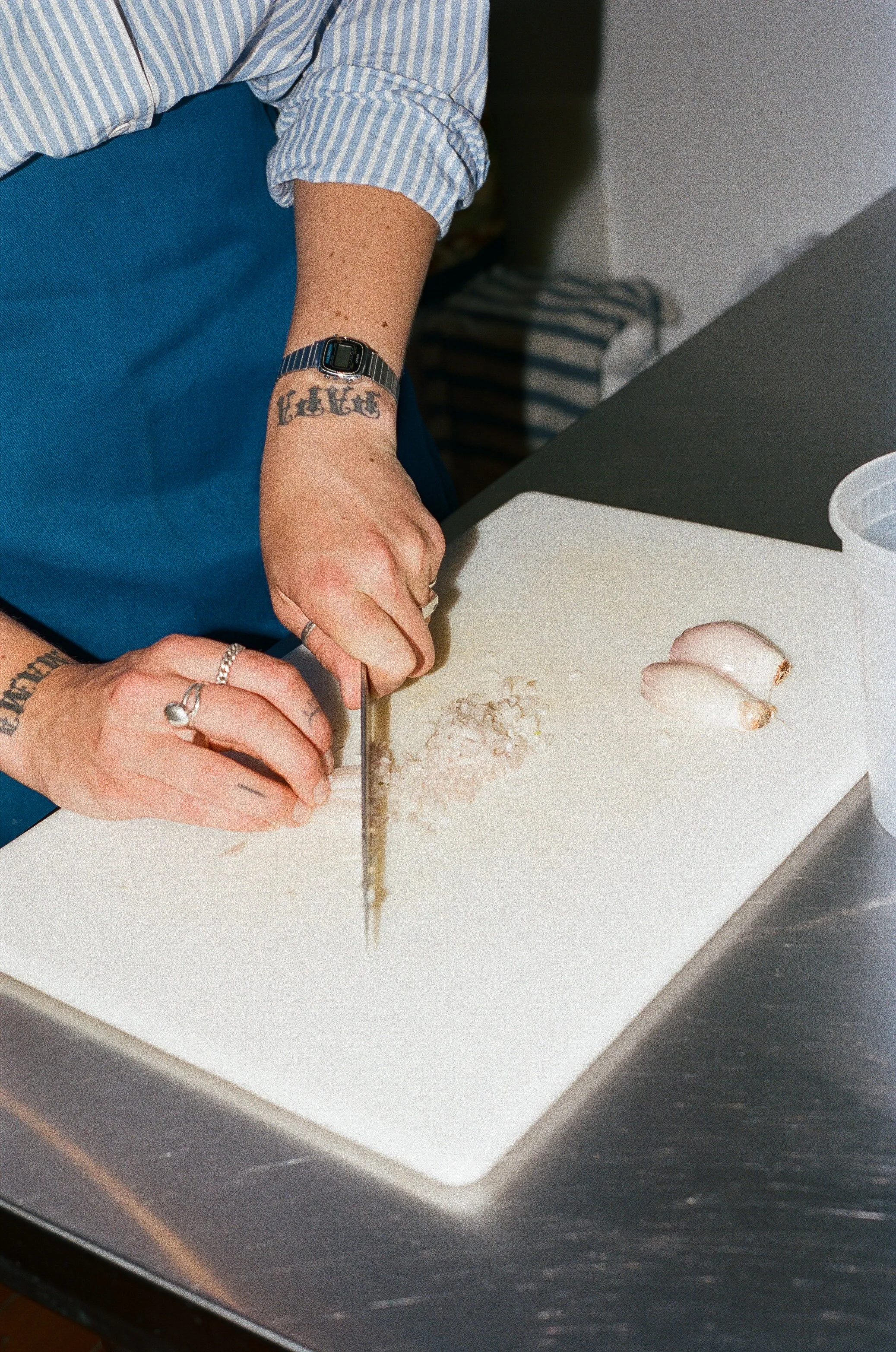Person chopping garlic on a white cutting board in a kitchen.