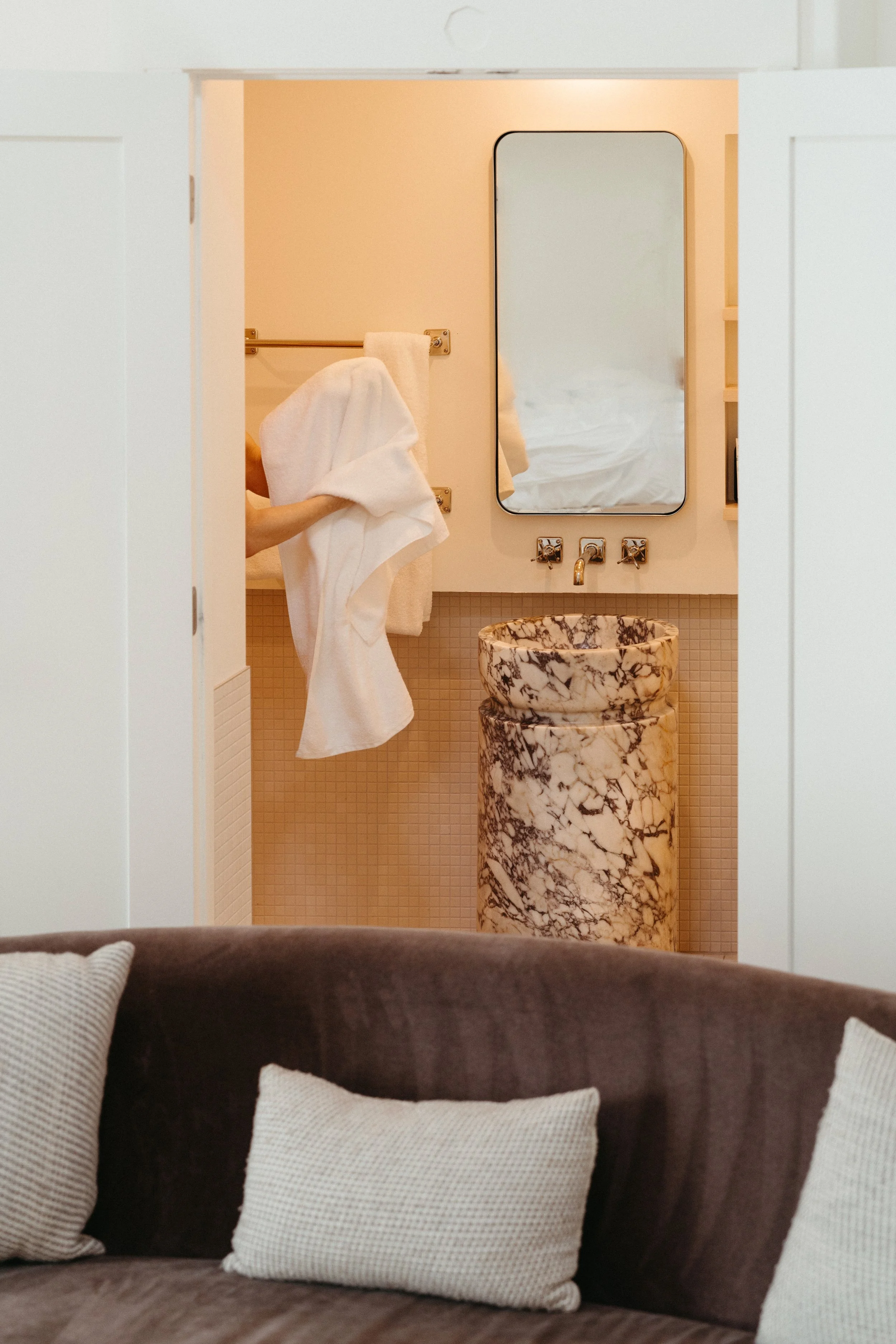 Person holding a white towel in a hotel bathroom with a marble sink and a mirror.