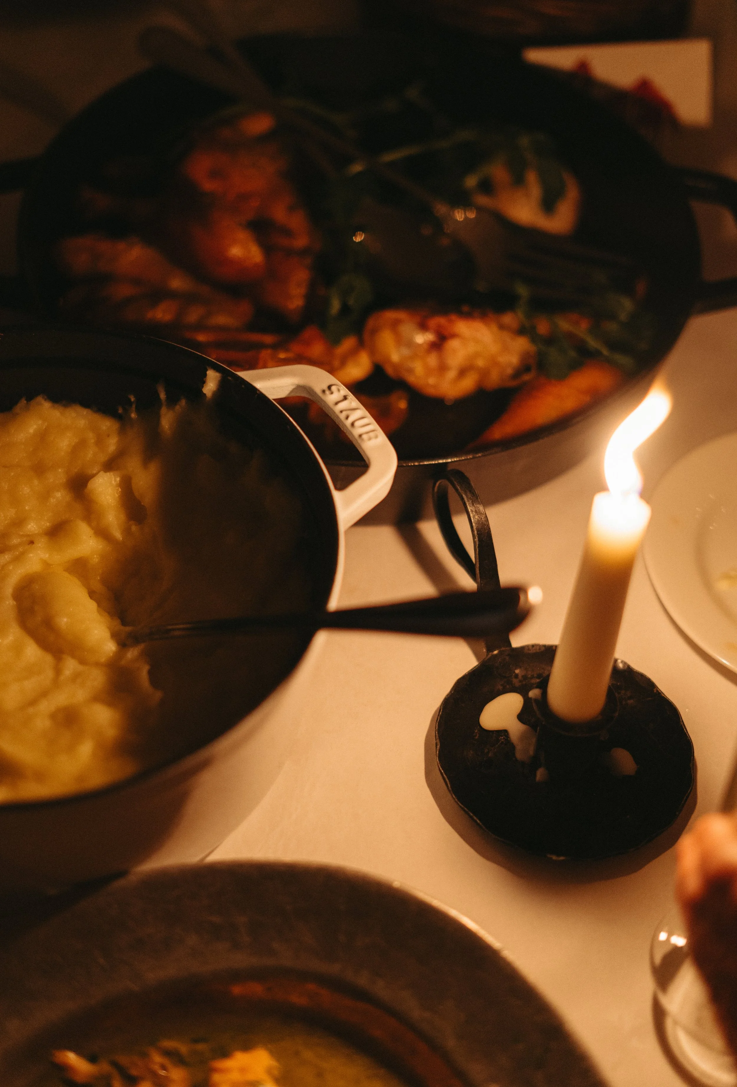 A dinner table with a lit candle, mashed potatoes, and a cast iron skillet with roasted chicken and vegetables.