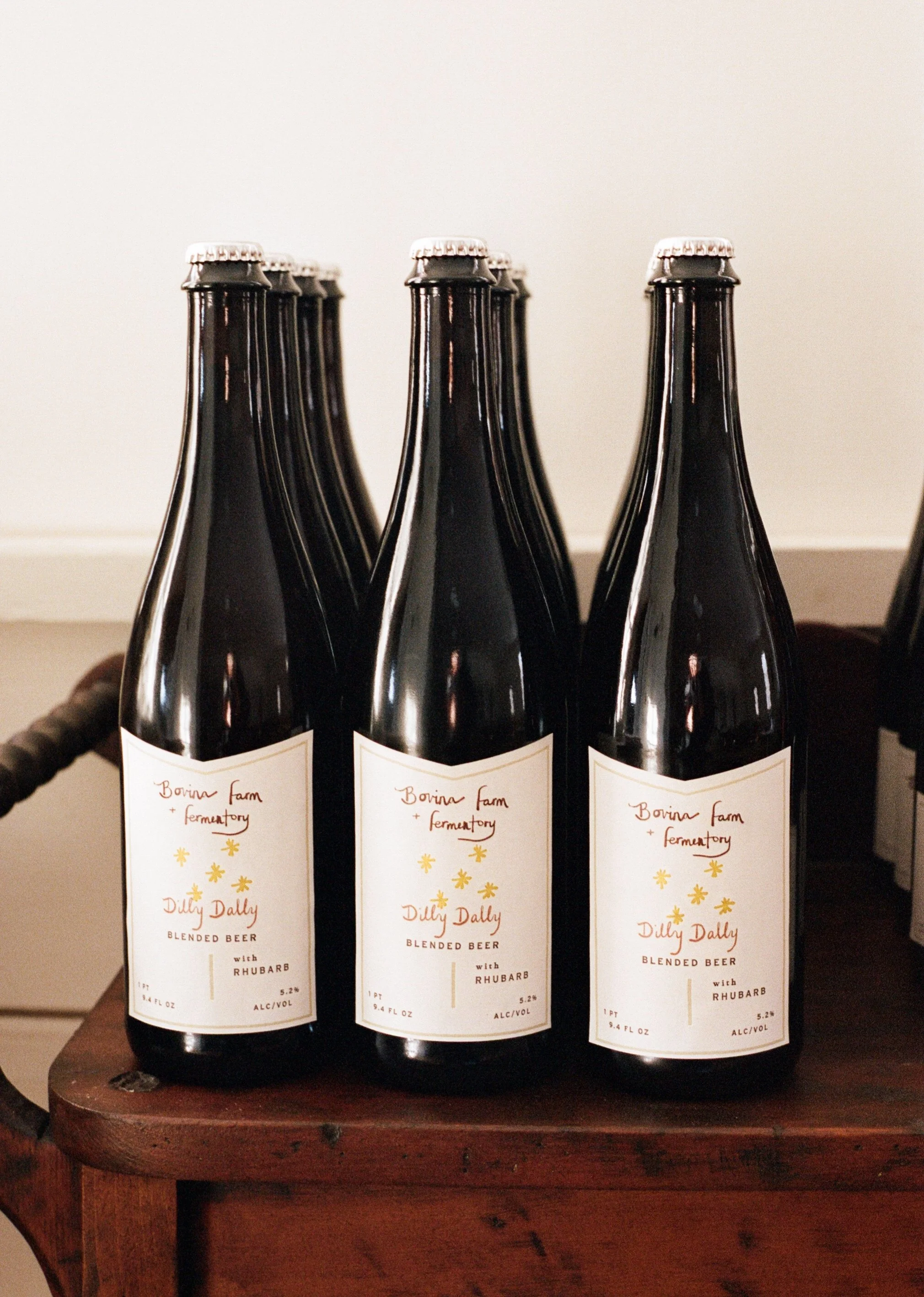 Three bottles of blended beer with rhubarb labeled "Dilly Dally," placed on a wooden surface.