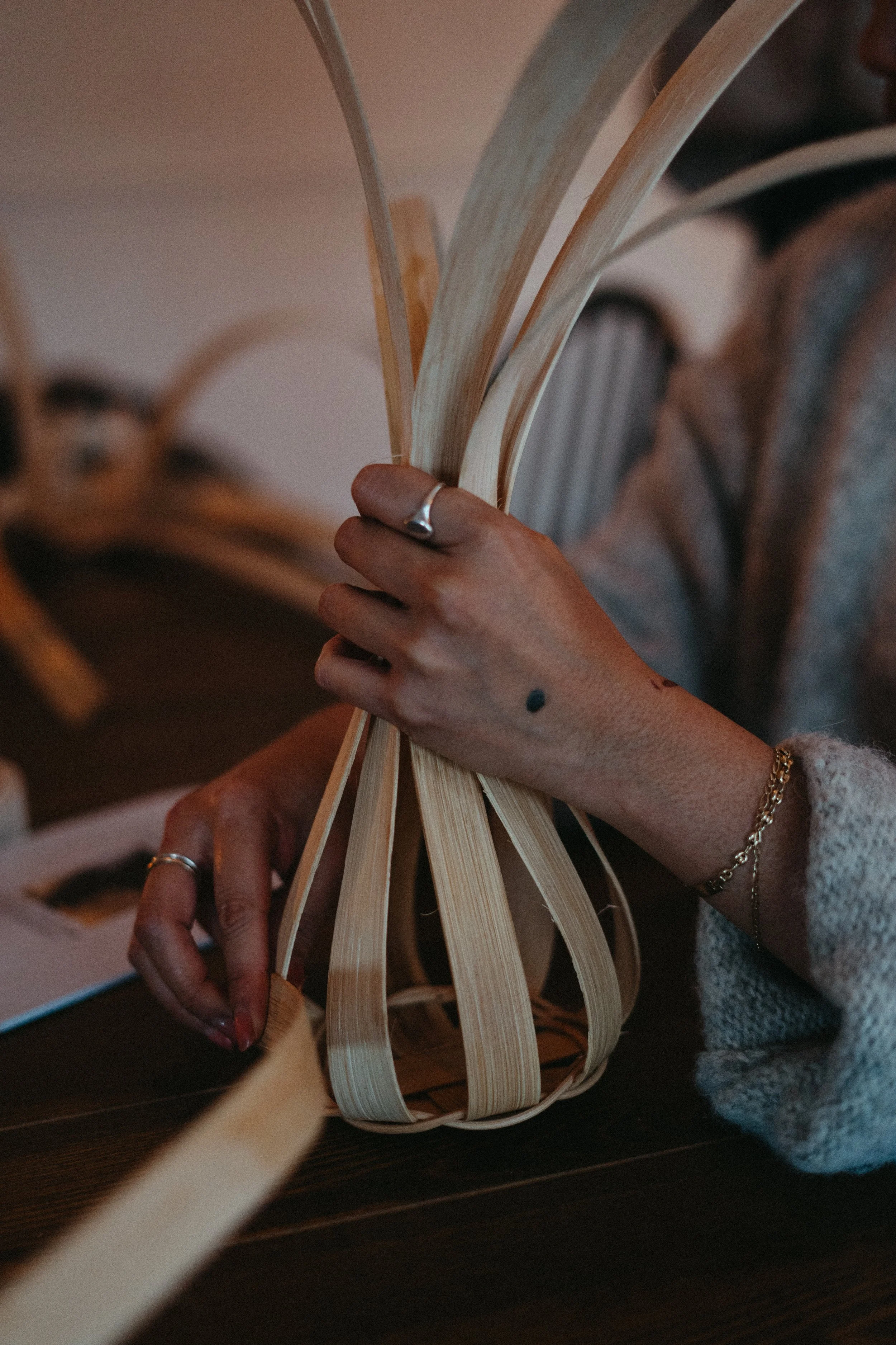 A person weaving a small basket with flat wooden strips.