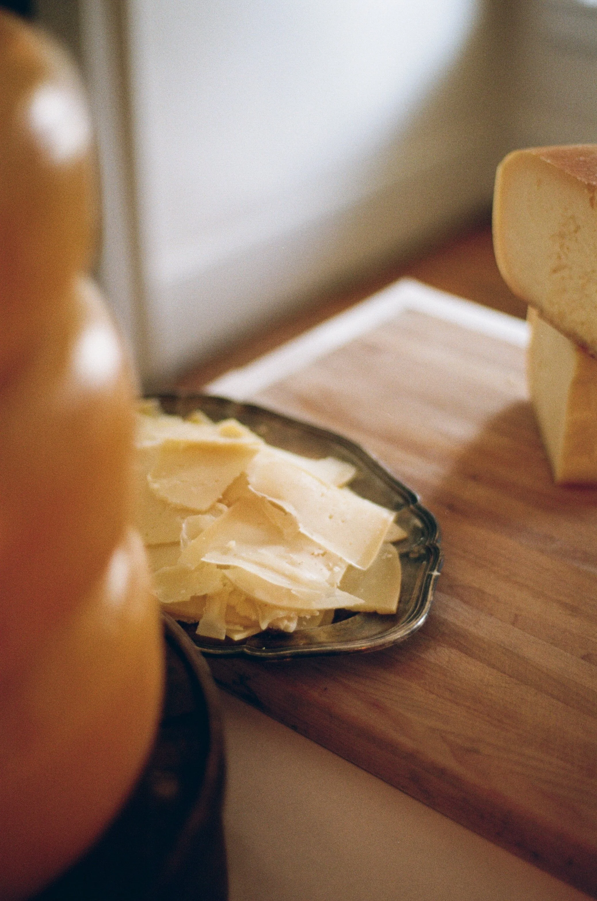 Slices of cheese on a glass dish and a block of cheese on a wooden cutting board.