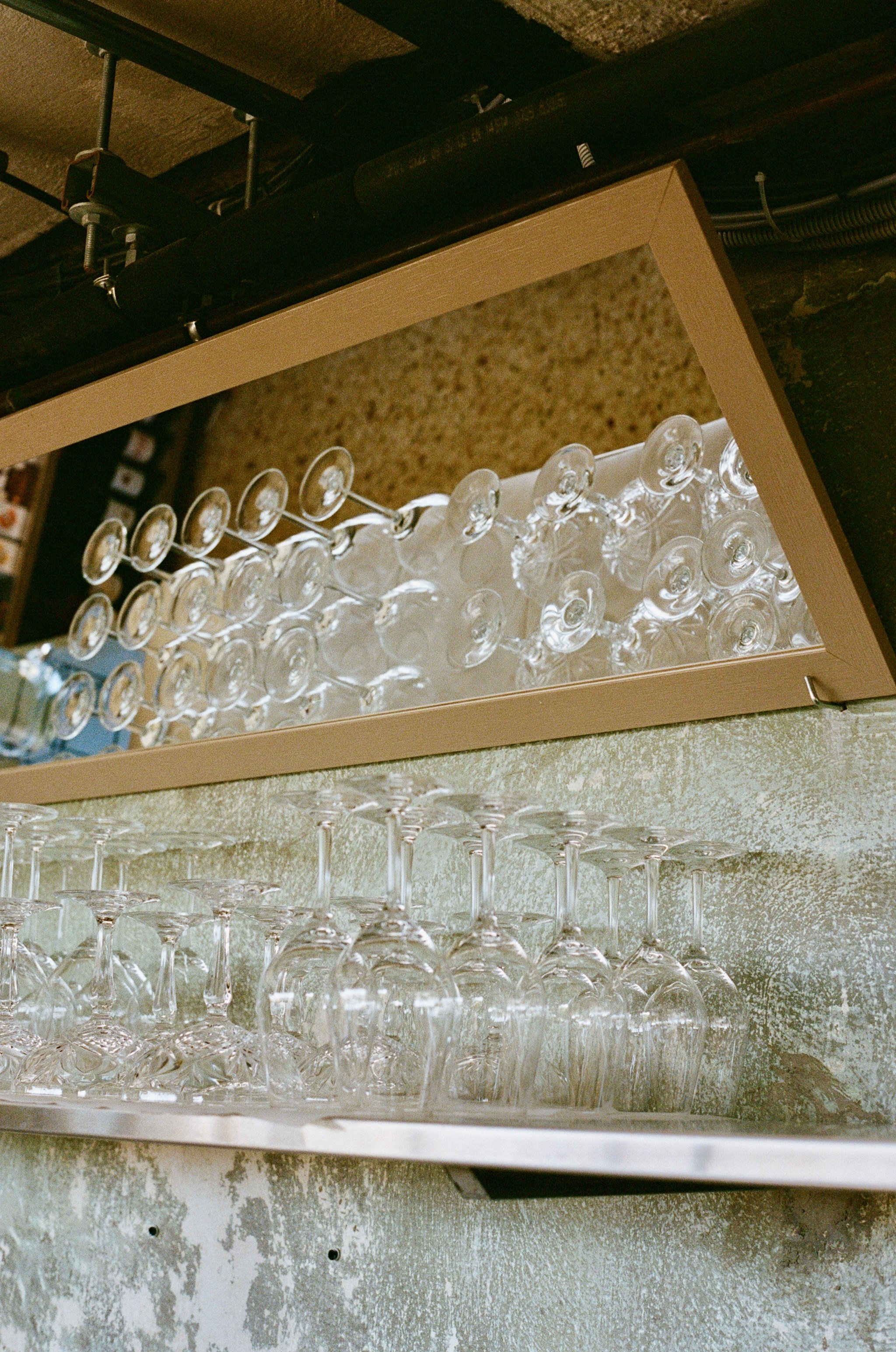 Rows of upside-down wine glasses on a metal shelf against a textured wall.