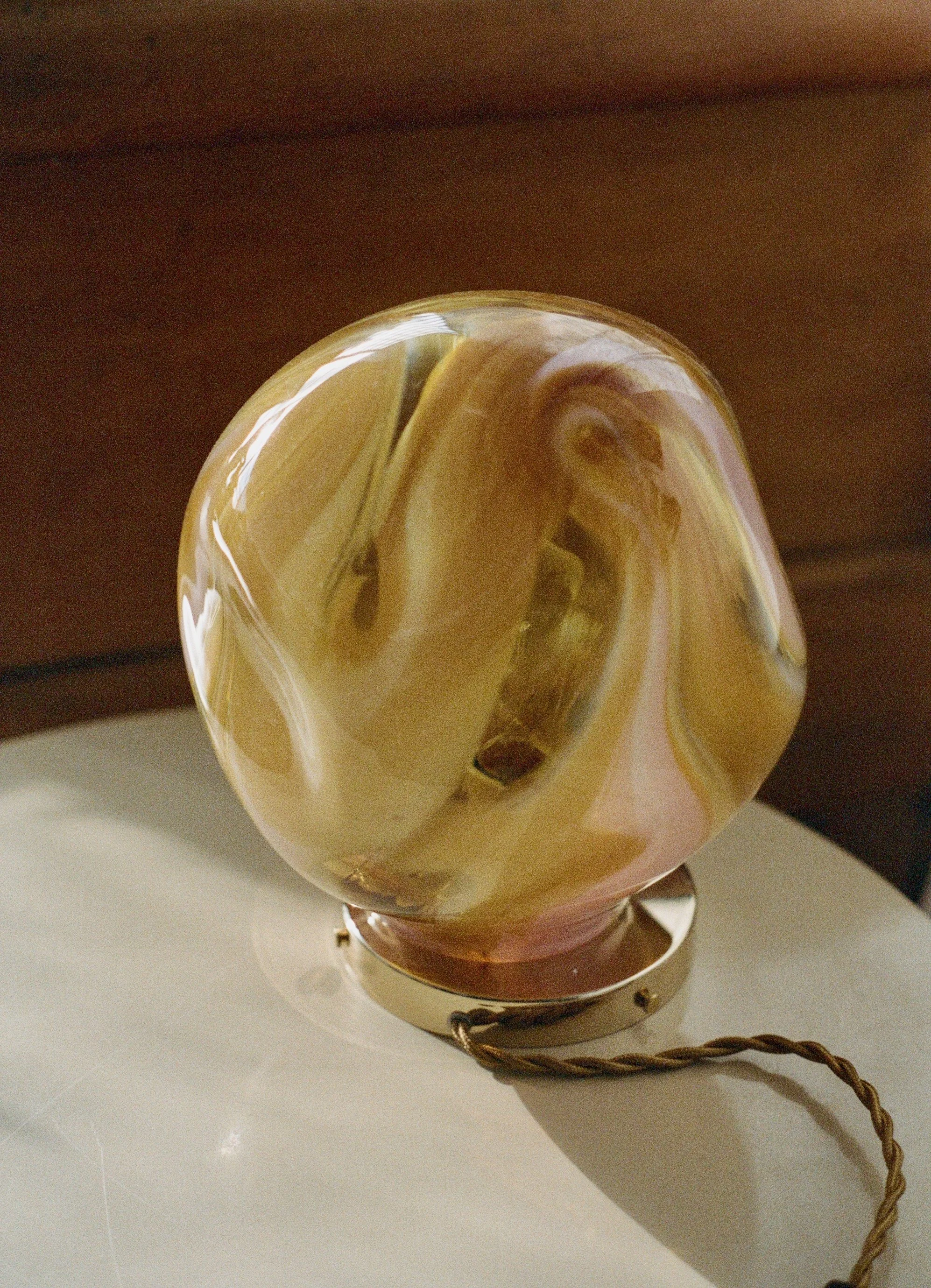 A decorative marble paperweight with swirling shades of yellow, cream, and gold, resting on a white surface with a brown background.