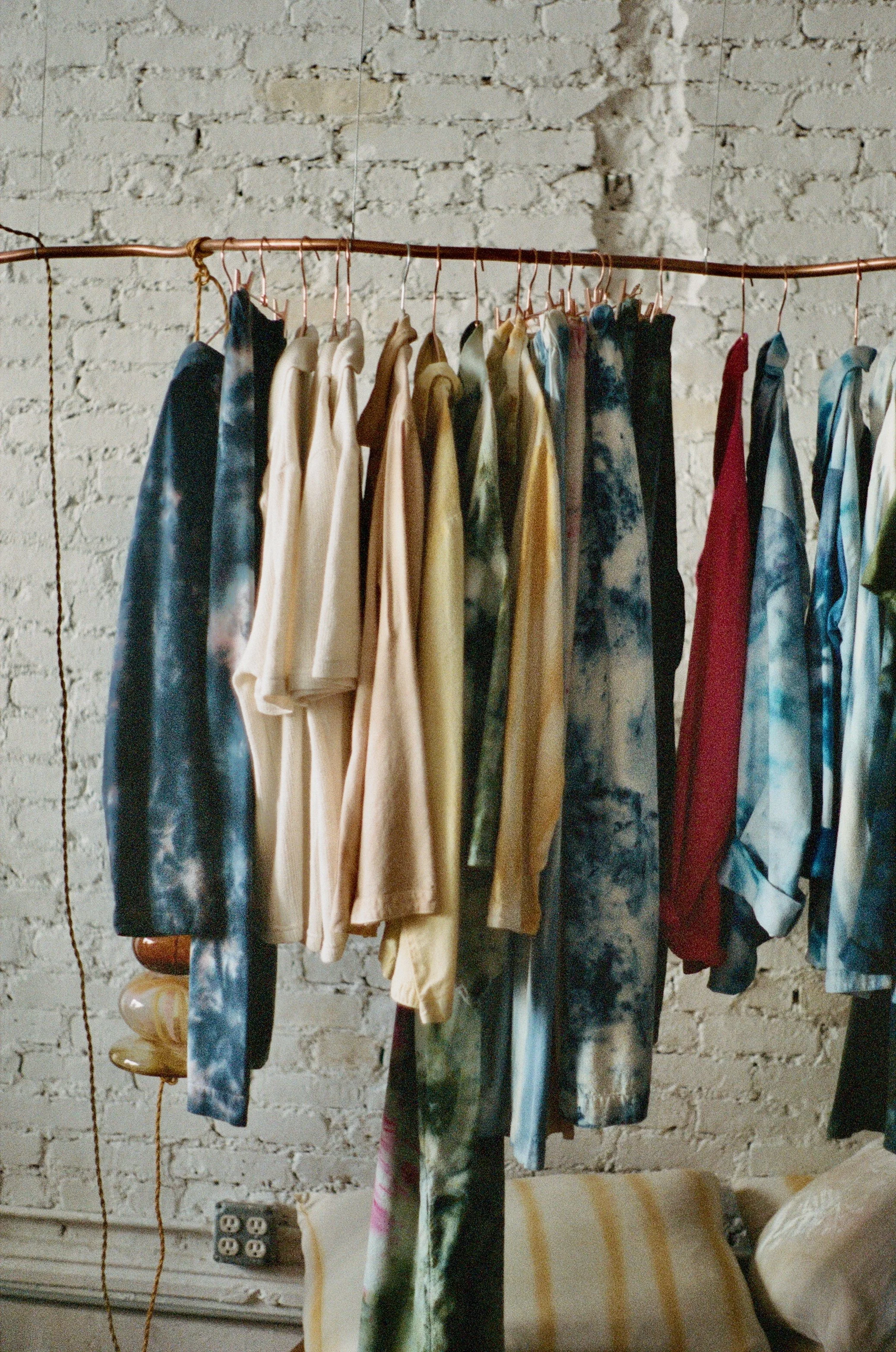 Clothes hanging on a copper clothing rack against a white brick wall.