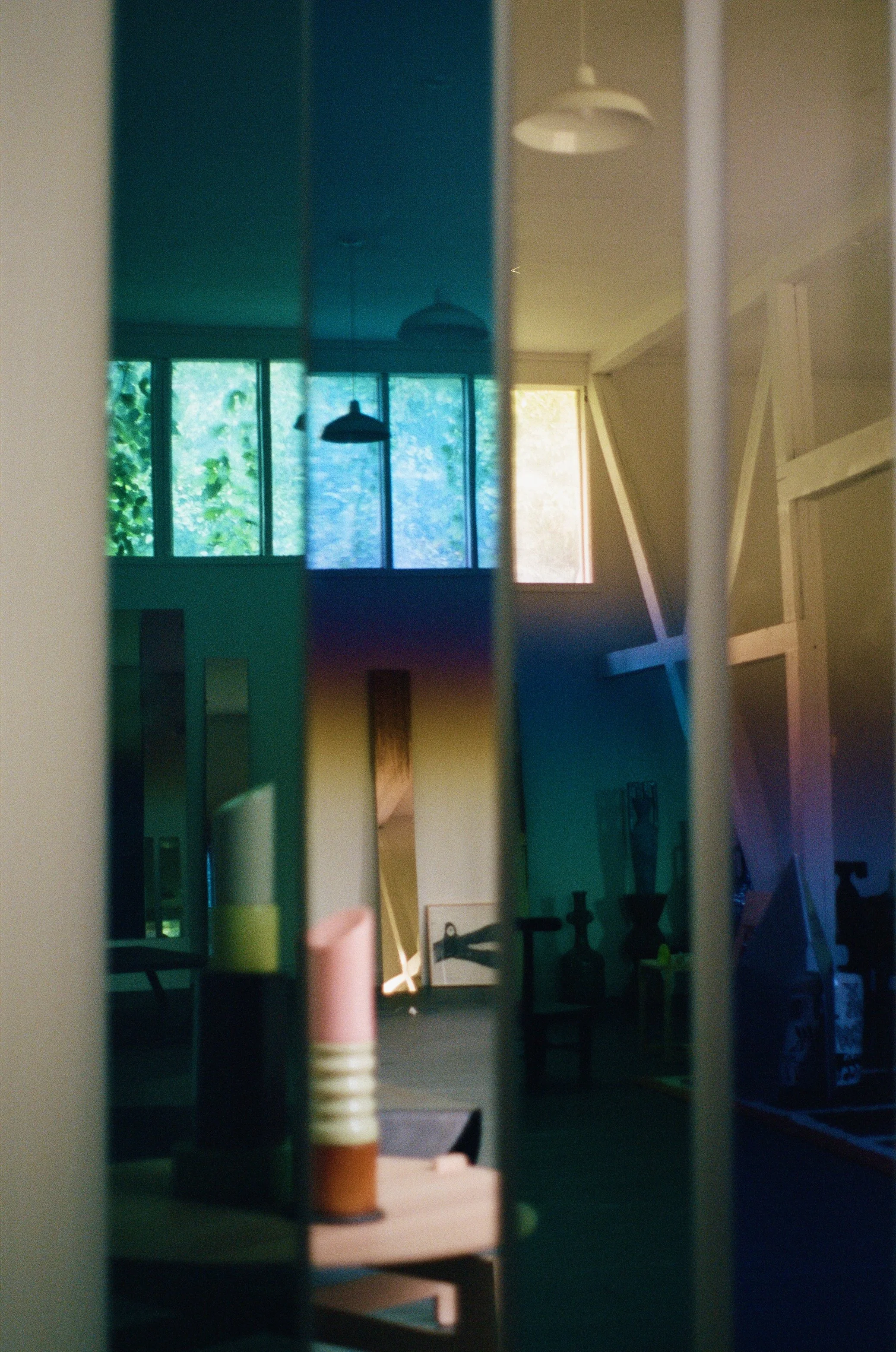 A mirror with multiple vertical panes reflecting the interior of a room with windows, a door, and various furniture and decor items.