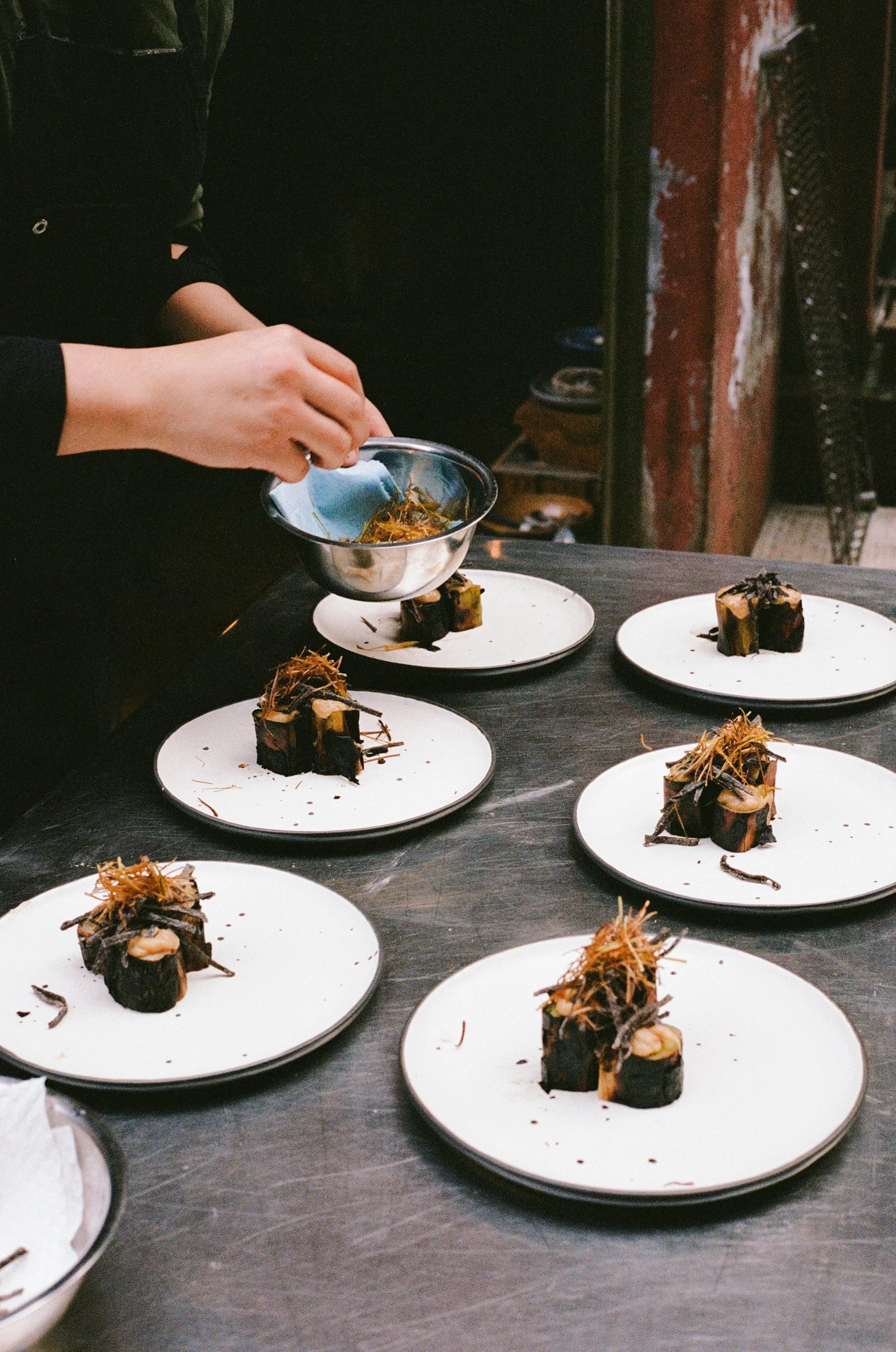 Chef garnishing plated gourmet desserts with caramelized topping.