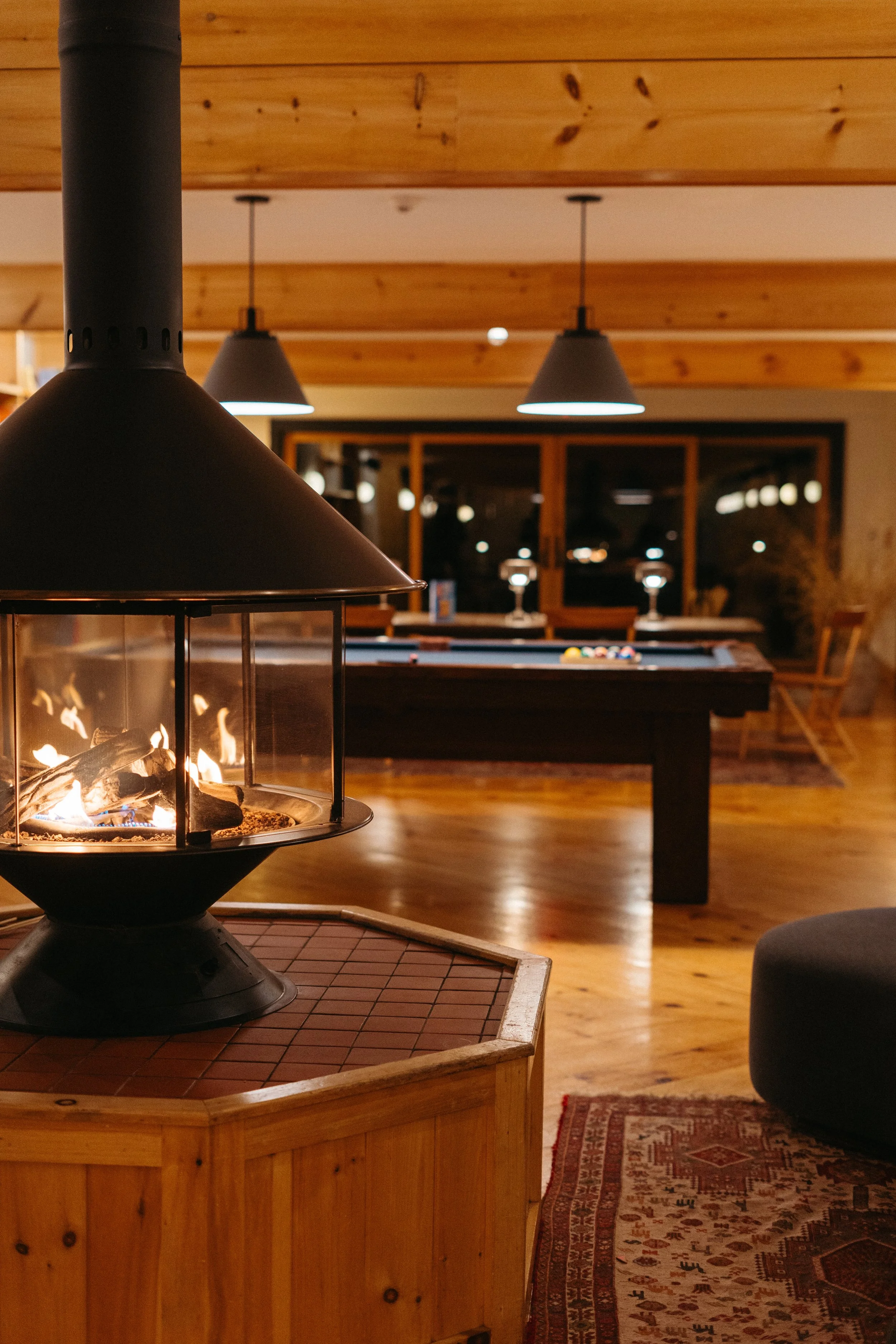 A cozy indoor scene with a lit fireplace, a pool table in the background, and warm wooden interior.