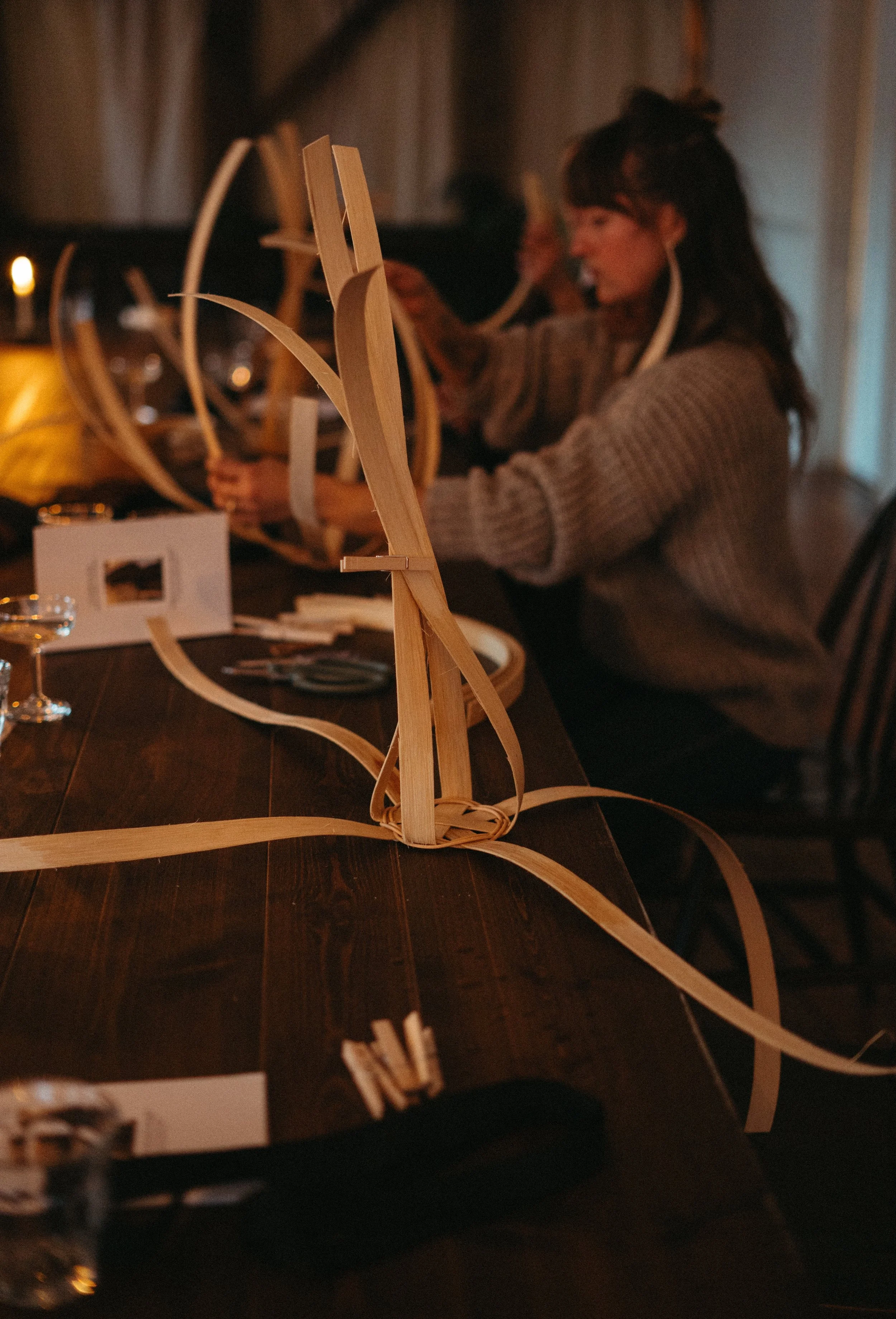 People creating or assembling wooden structures or art pieces at a table in a dimly lit room.