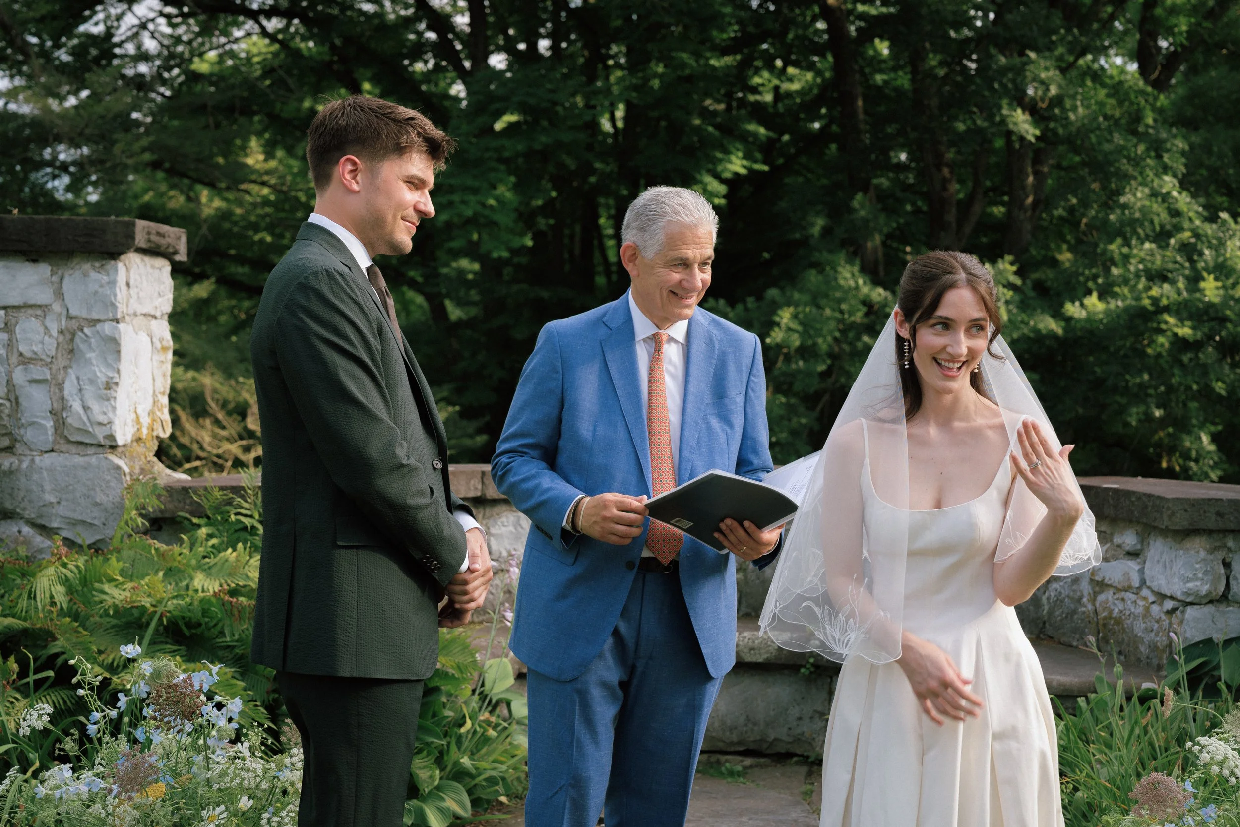 A bride, groom, and their officiant looking joyful after their ring exchanges